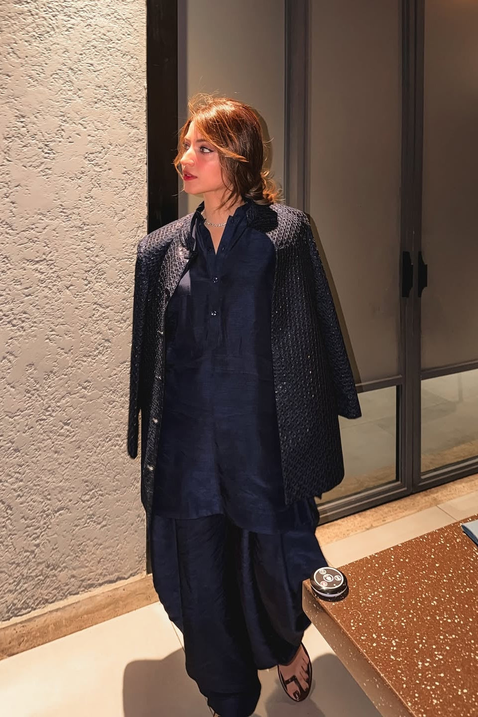 Woman in a navy outfit standing in a room with a textured wall and glass door.