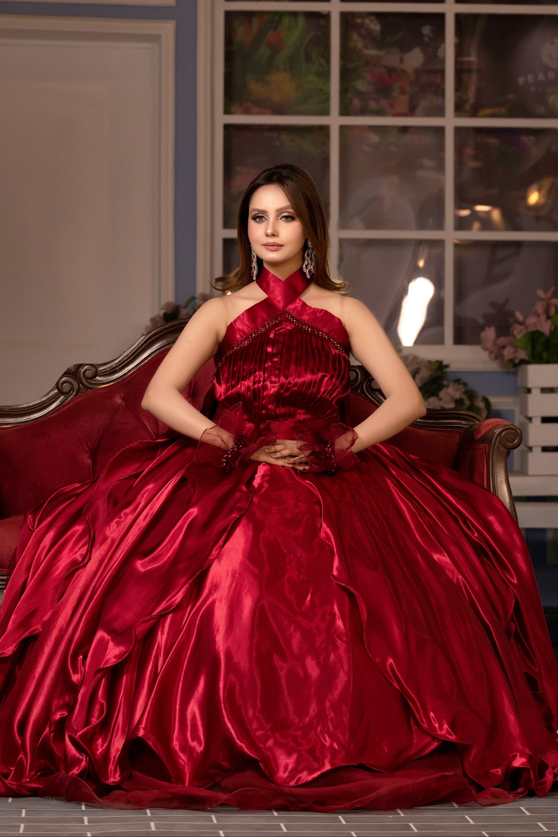 Woman in a red gown sitting on a decorative chair in an indoor setting.