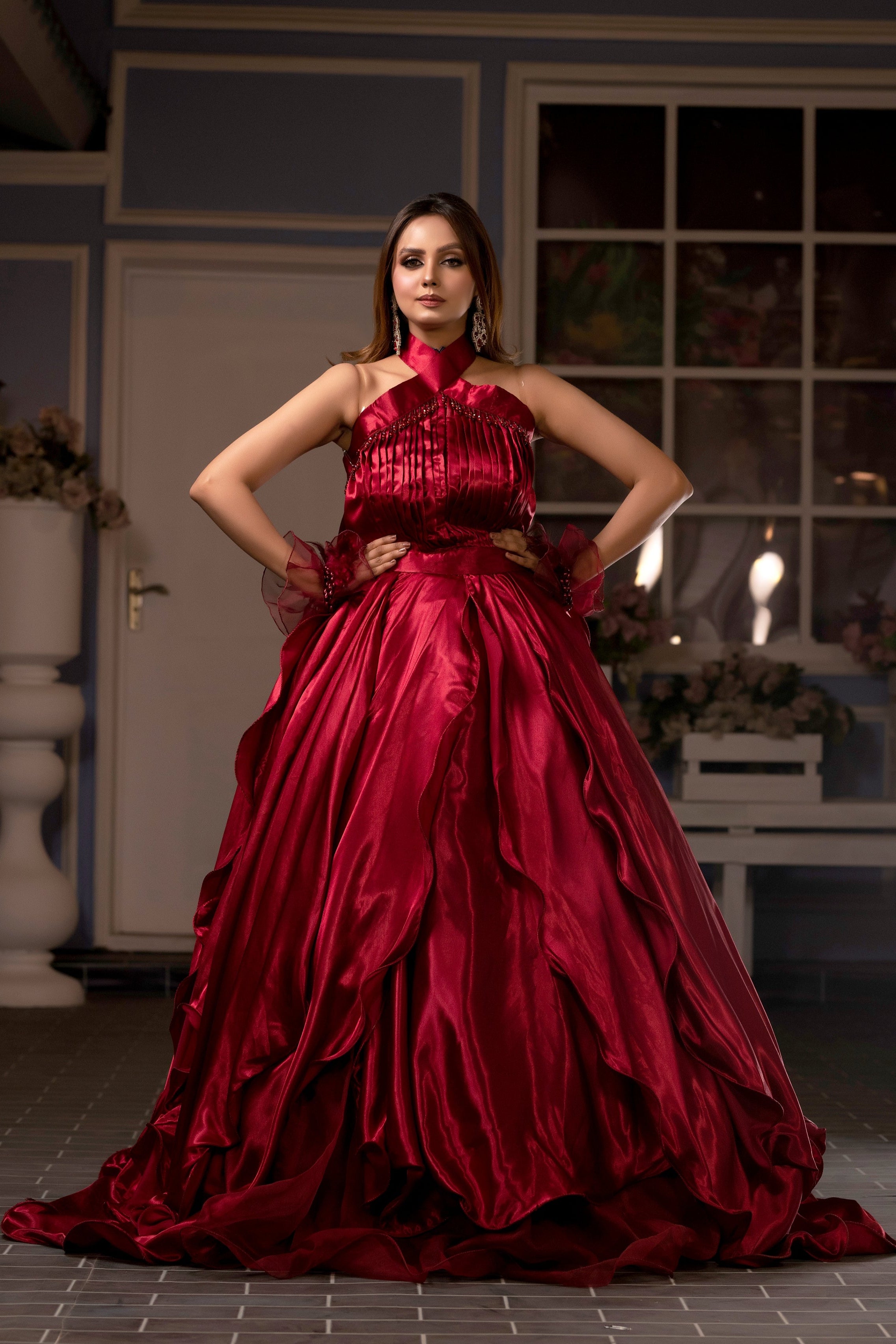 Woman in a red evening gown standing in an elegant indoor setting.