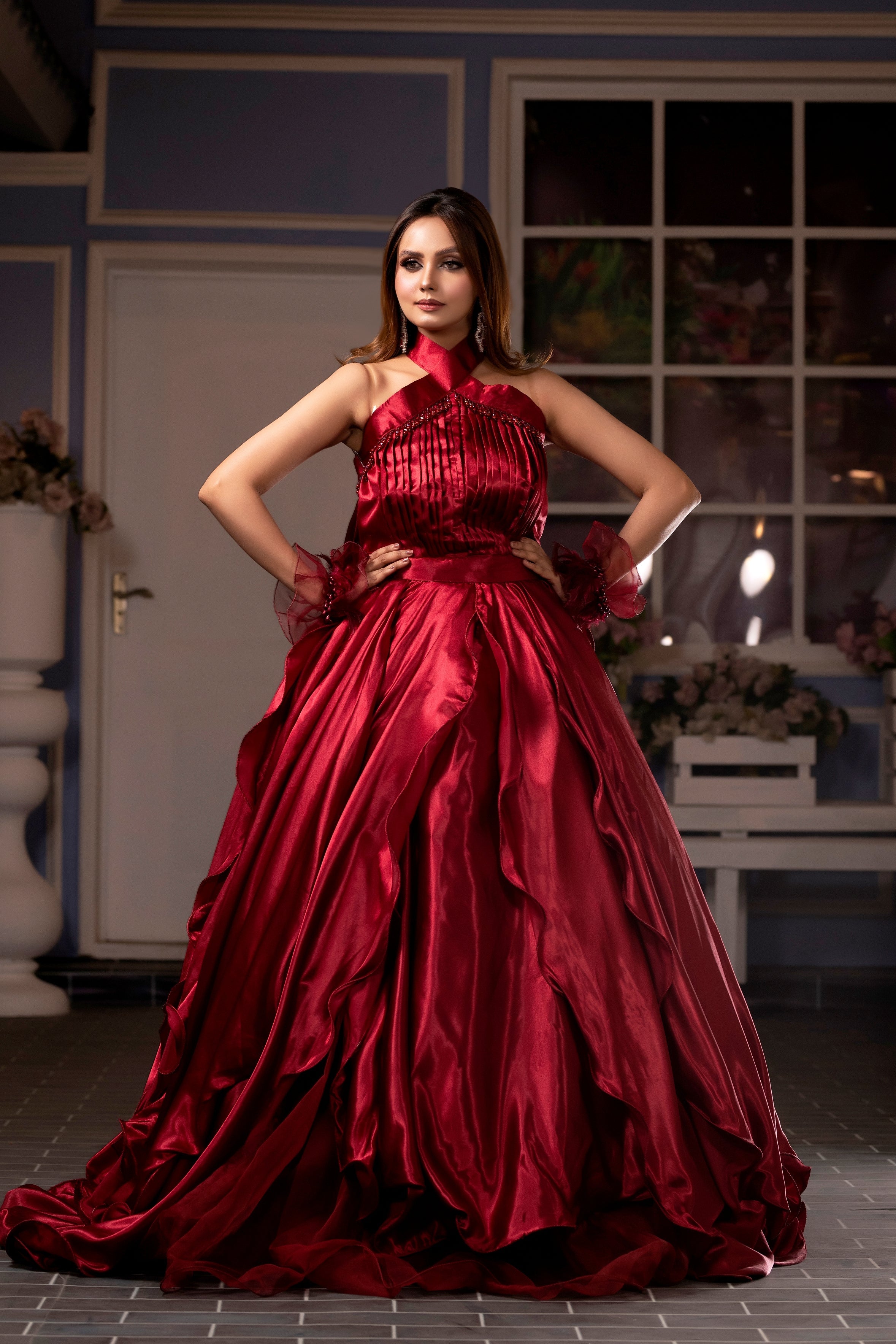 Woman in a red evening gown standing in an outdoor setting with decorative elements.