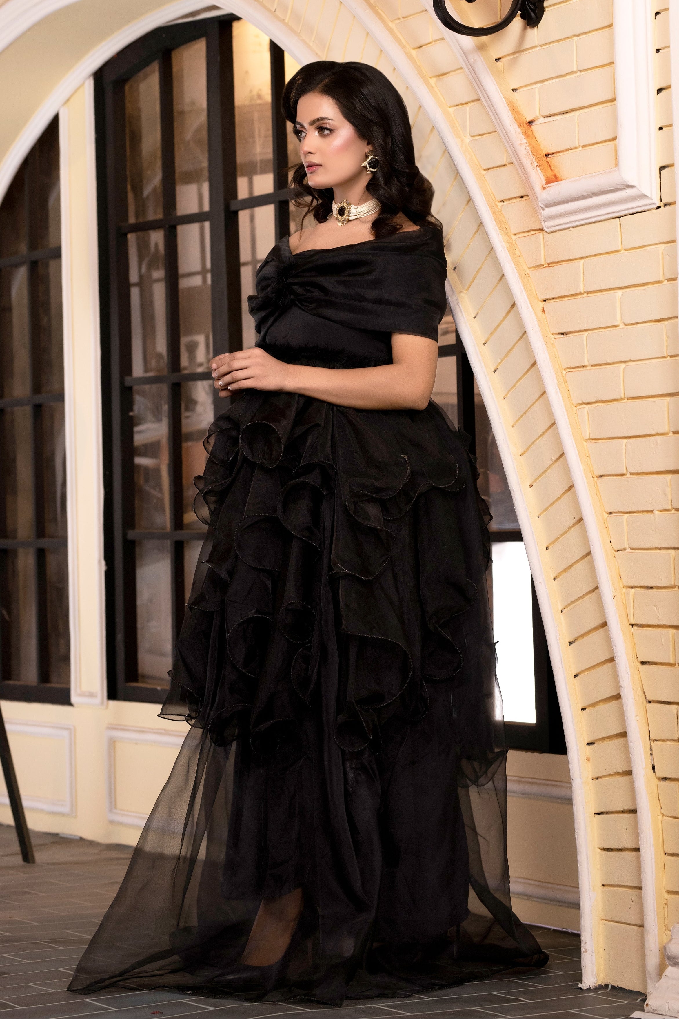 Woman wearing a black ruffled dress standing in an elegant interior setting.