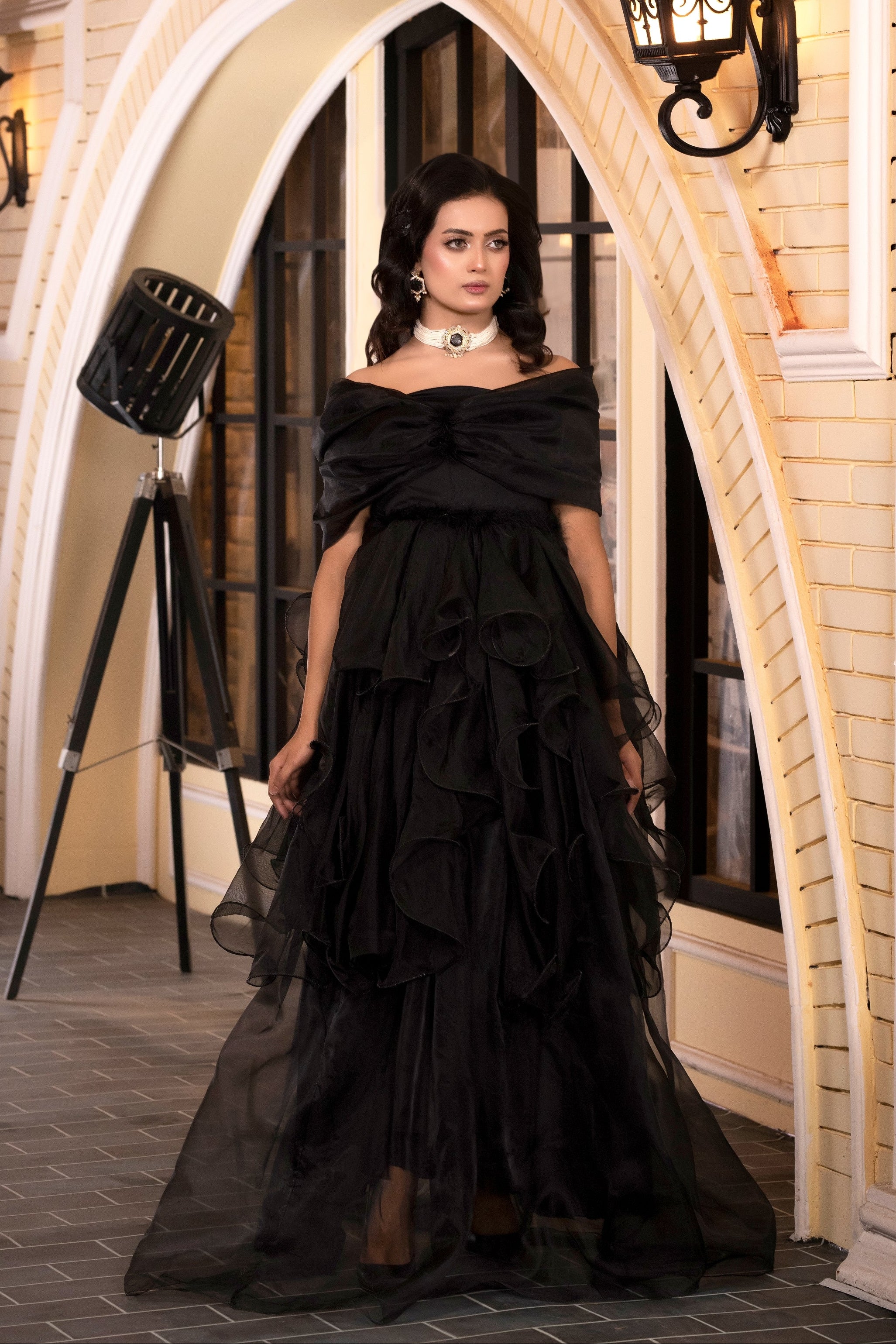 Woman in a black off-shoulder gown standing in an elegant interior setting.