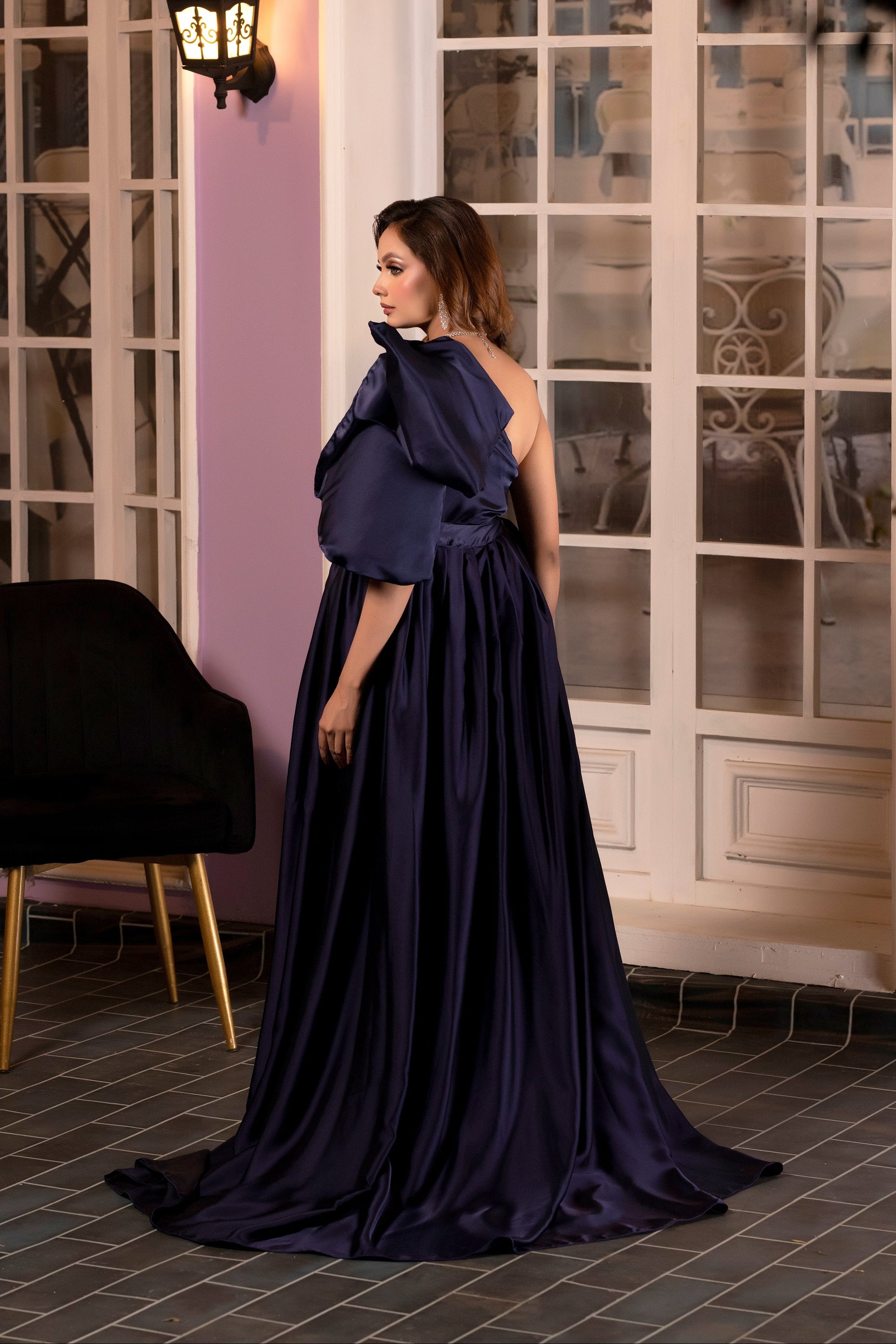 Woman in a navy blue evening gown standing in an elegant room with purple walls and glass doors.