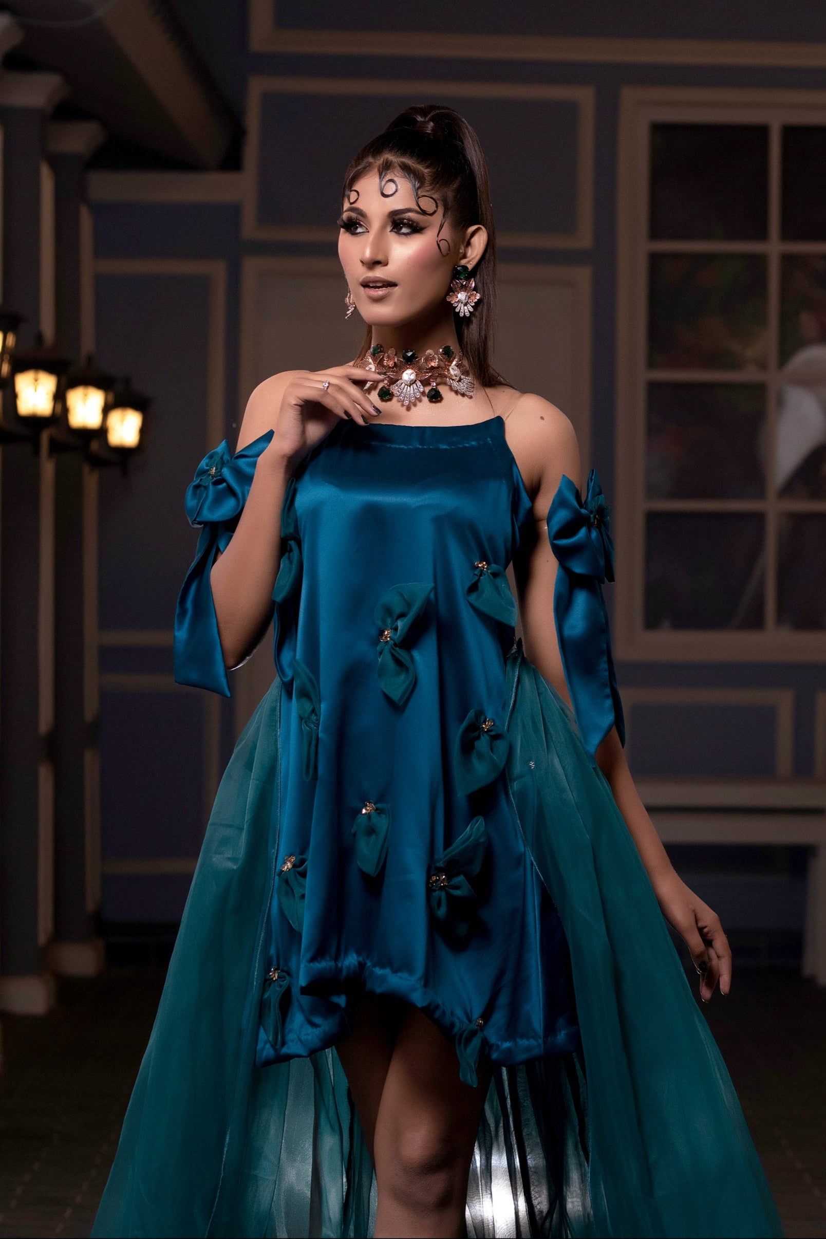 Woman in a blue dress standing in an indoor setting with decorative elements.