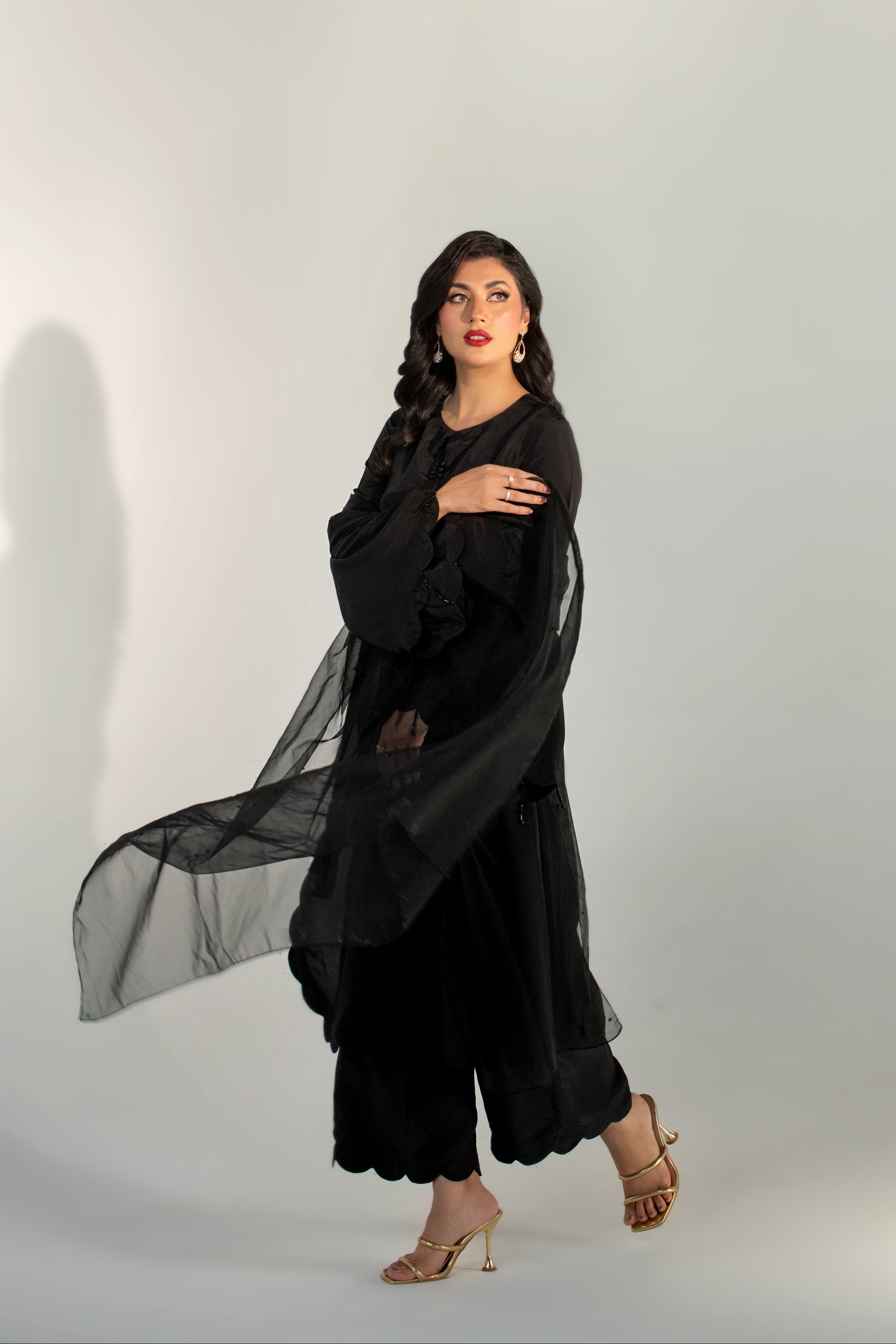 Woman wearing a black outfit with a sheer overlay against a white background