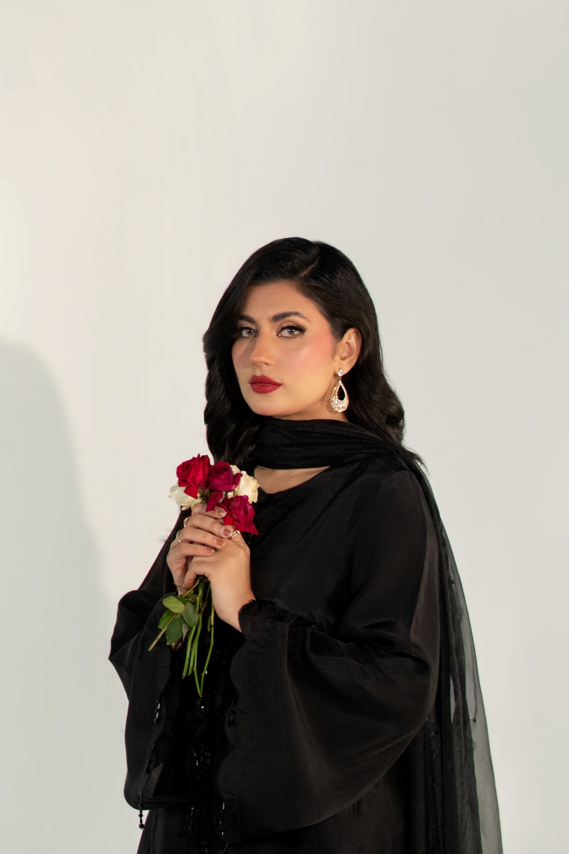 Woman in black outfit holding a red flower against a white background