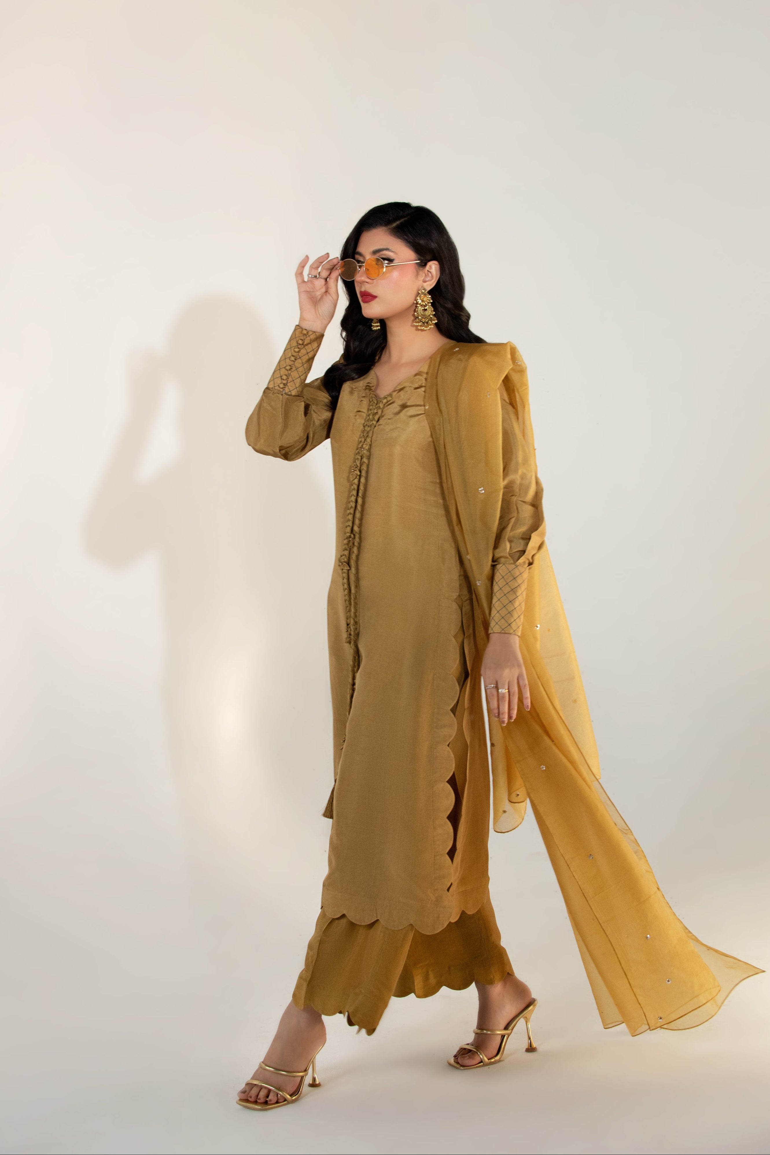 Woman wearing a mustard yellow outfit with a long jacket and pants on a white background