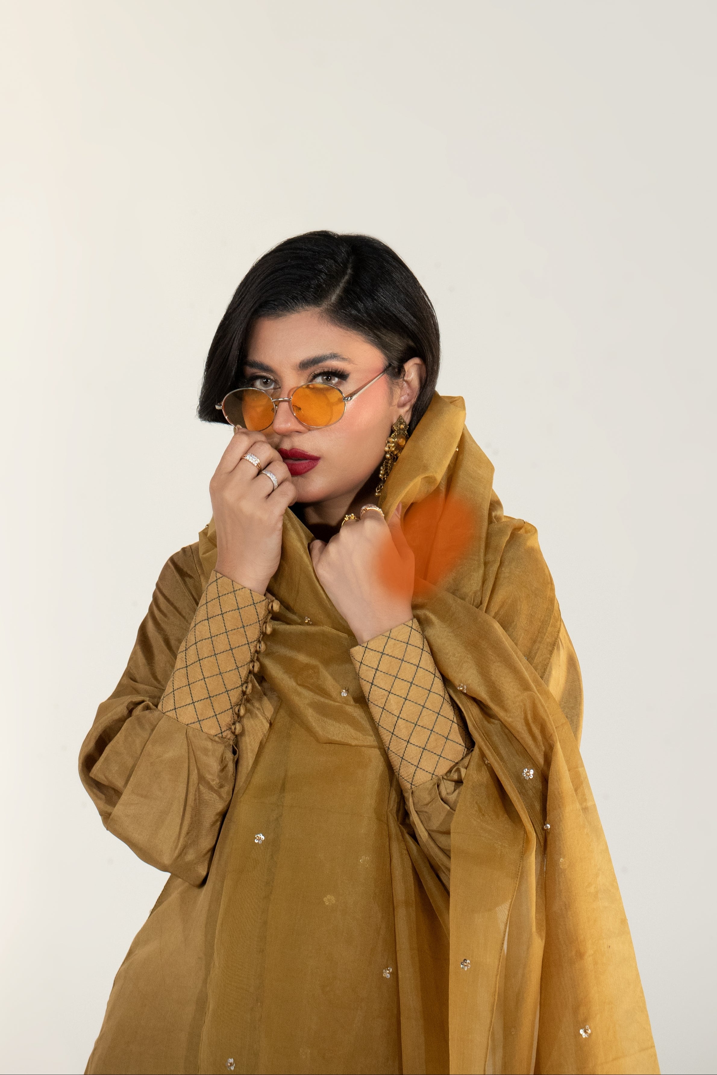 Woman wearing a mustard yellow outfit with sunglasses against a white background