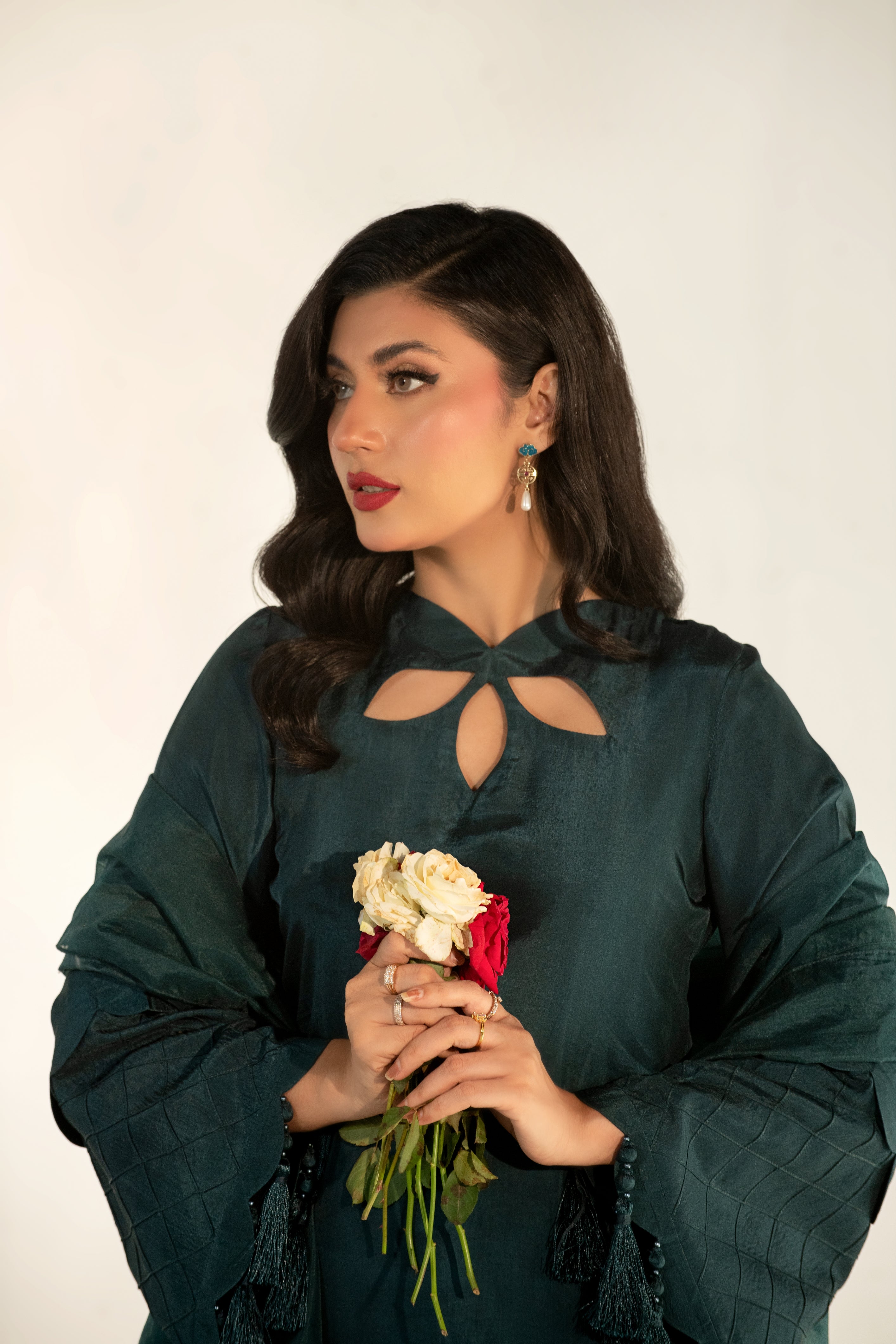Woman in a dark green outfit holding flowers against a white background