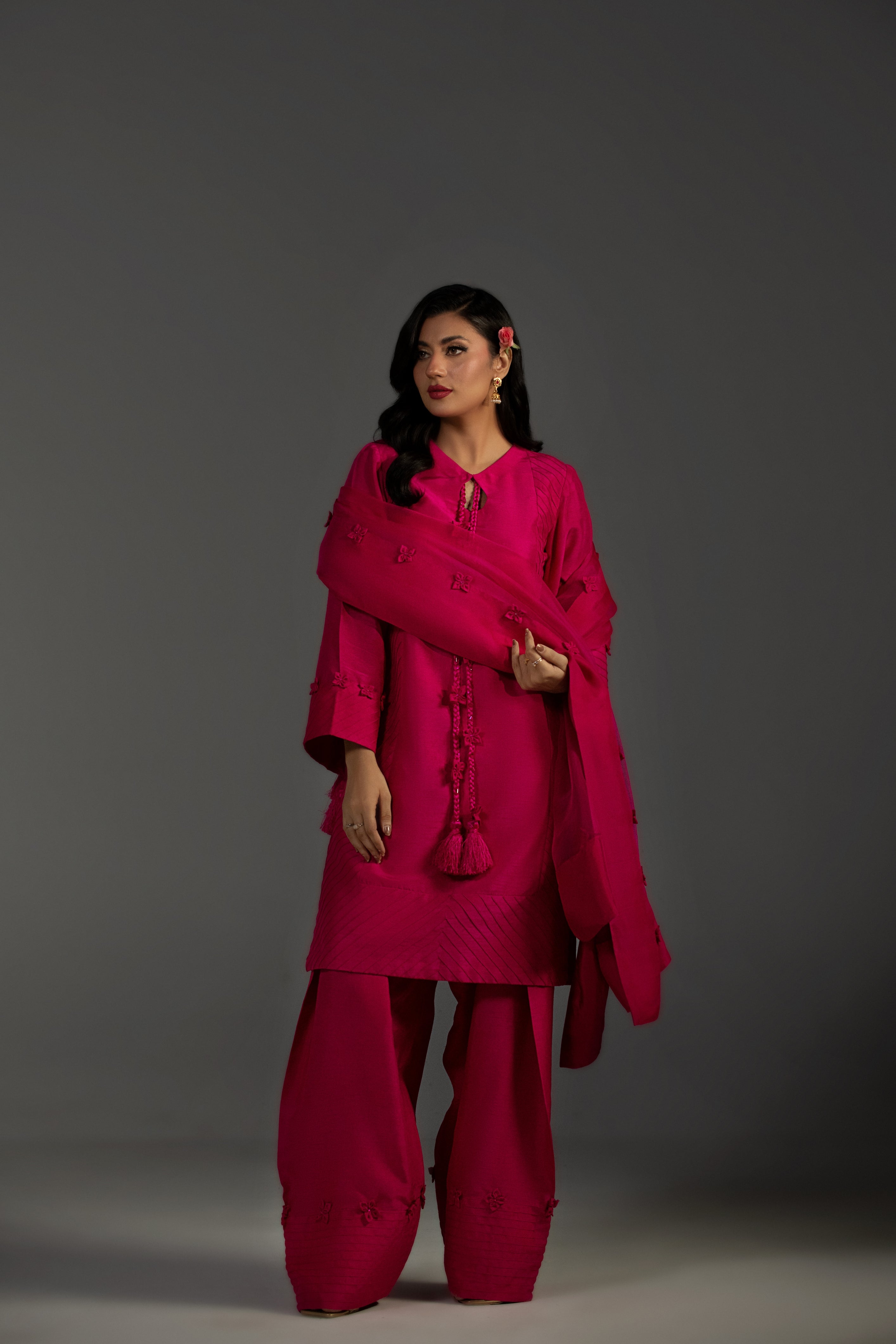 Woman wearing a bright pink traditional outfit with a shawl against a gray background