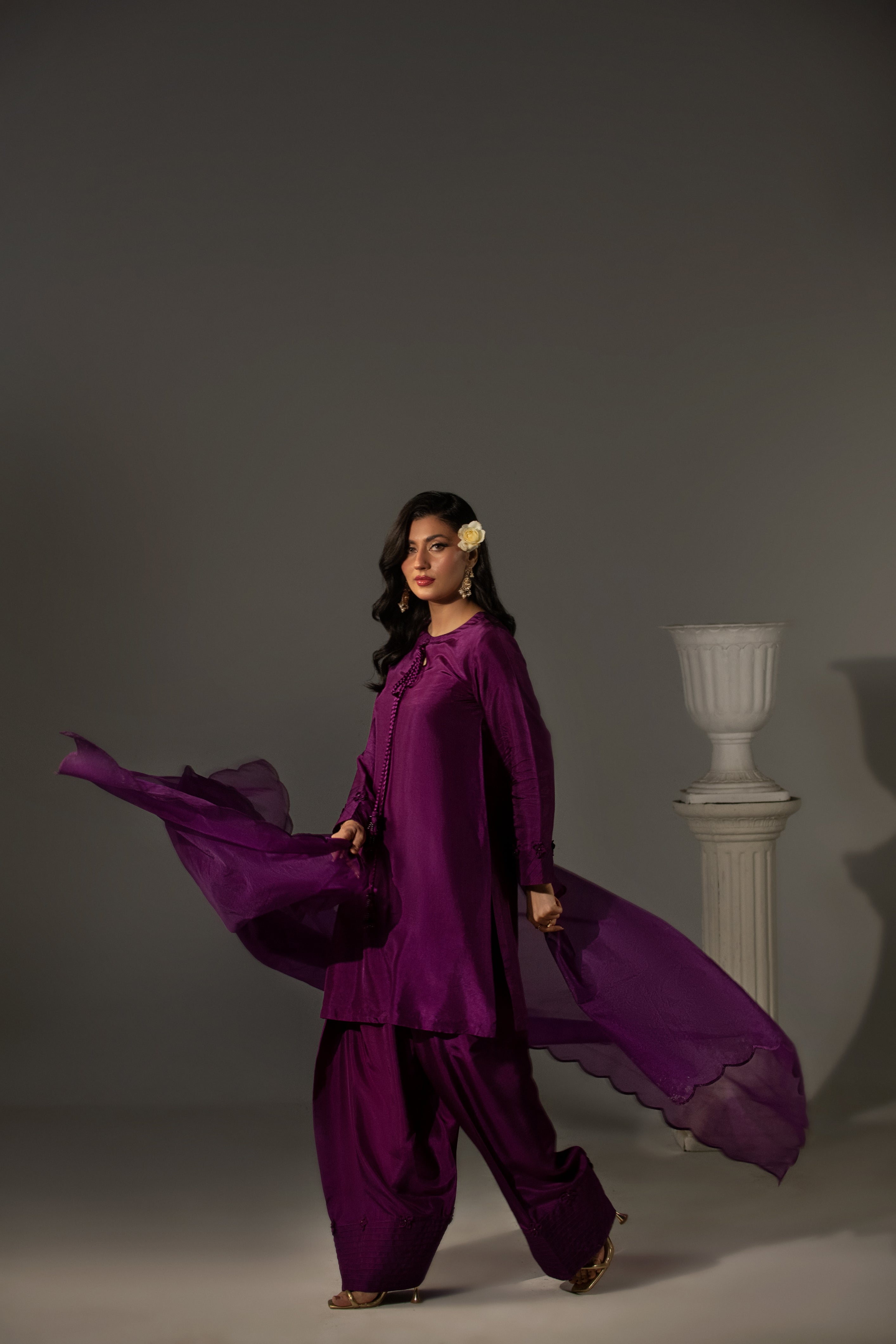 Woman in a flowing purple outfit against a gray background