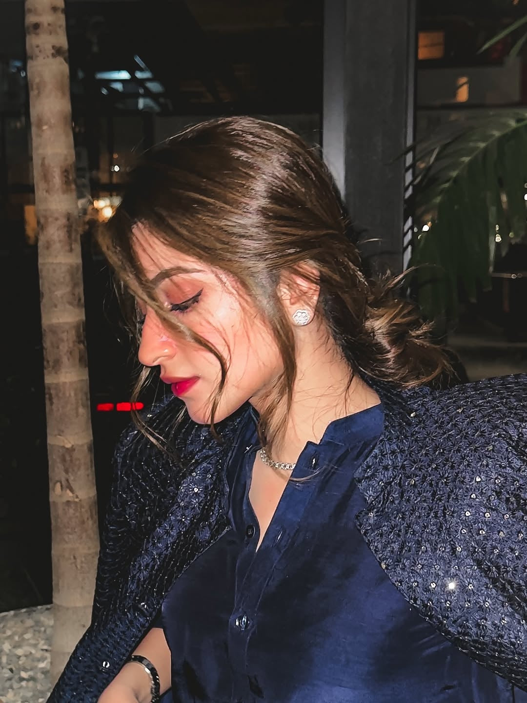 Woman with a ponytail wearing a blue top and dark jacket indoors