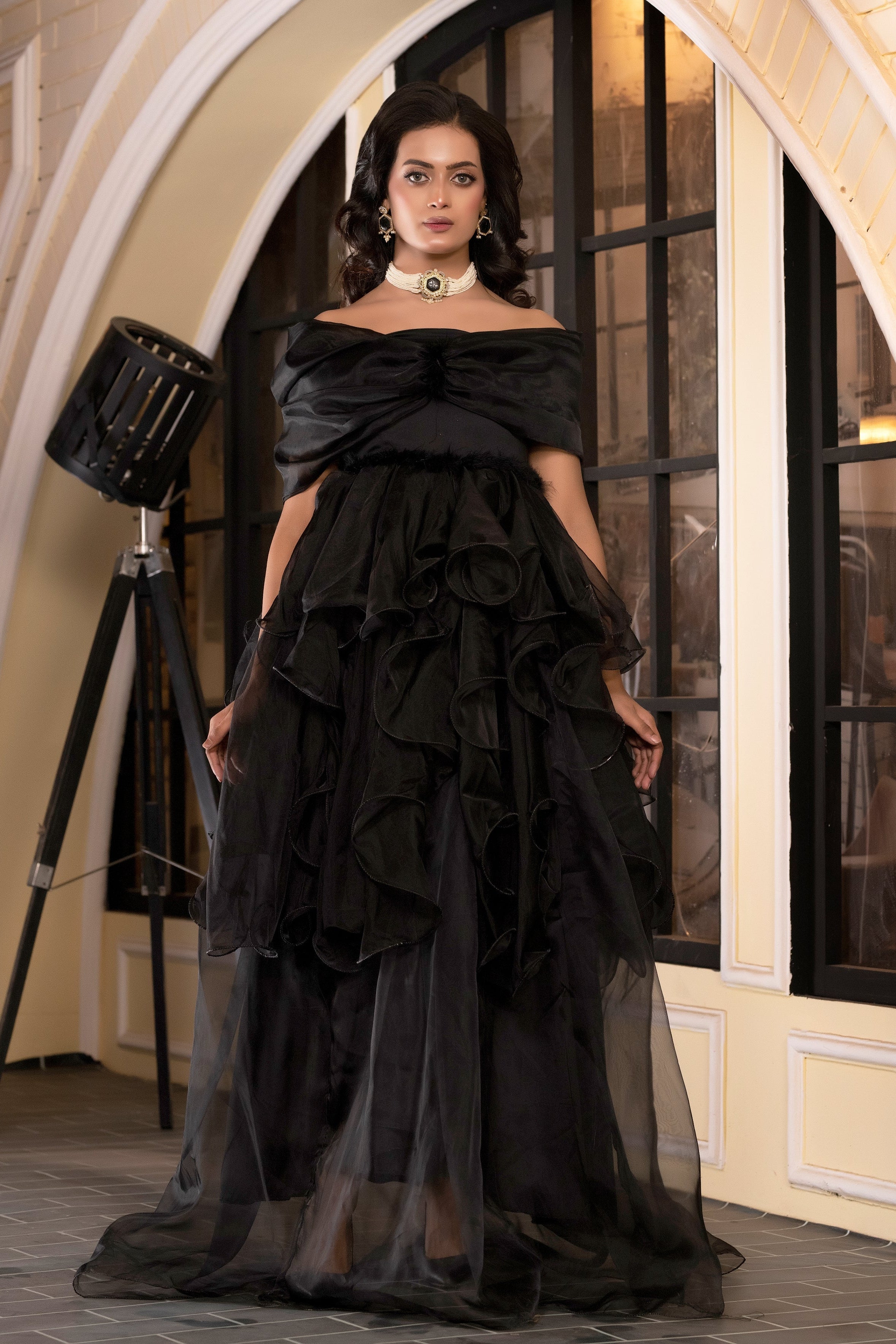 Woman in a black ruffled gown standing in an elegant interior setting.