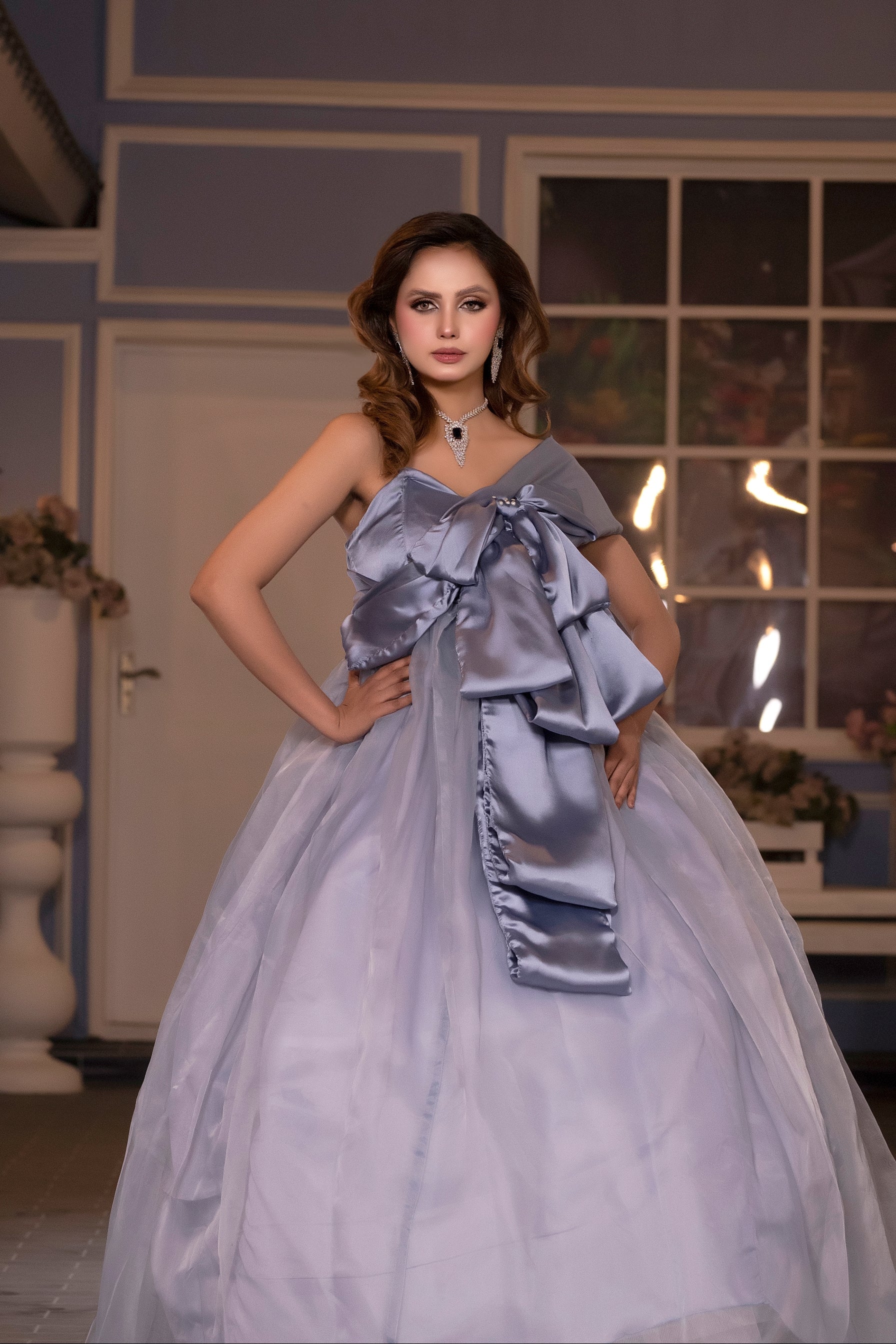 Woman in a light blue evening gown standing in an outdoor setting with decorative elements.