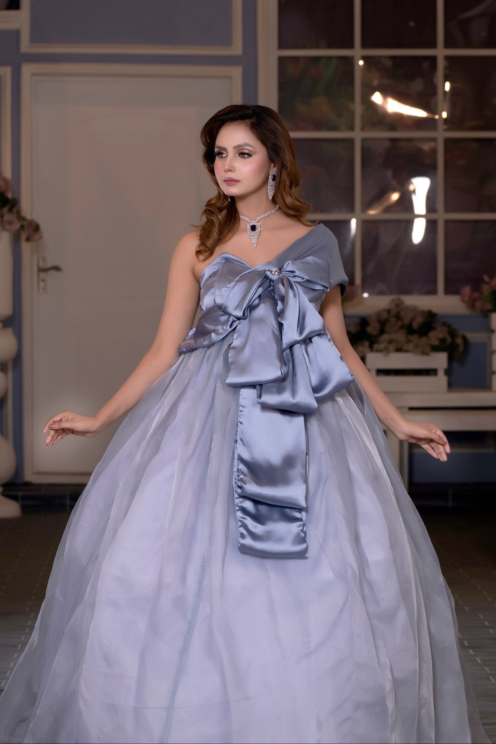 Woman in a light blue gown with a large bow standing in an indoor setting.