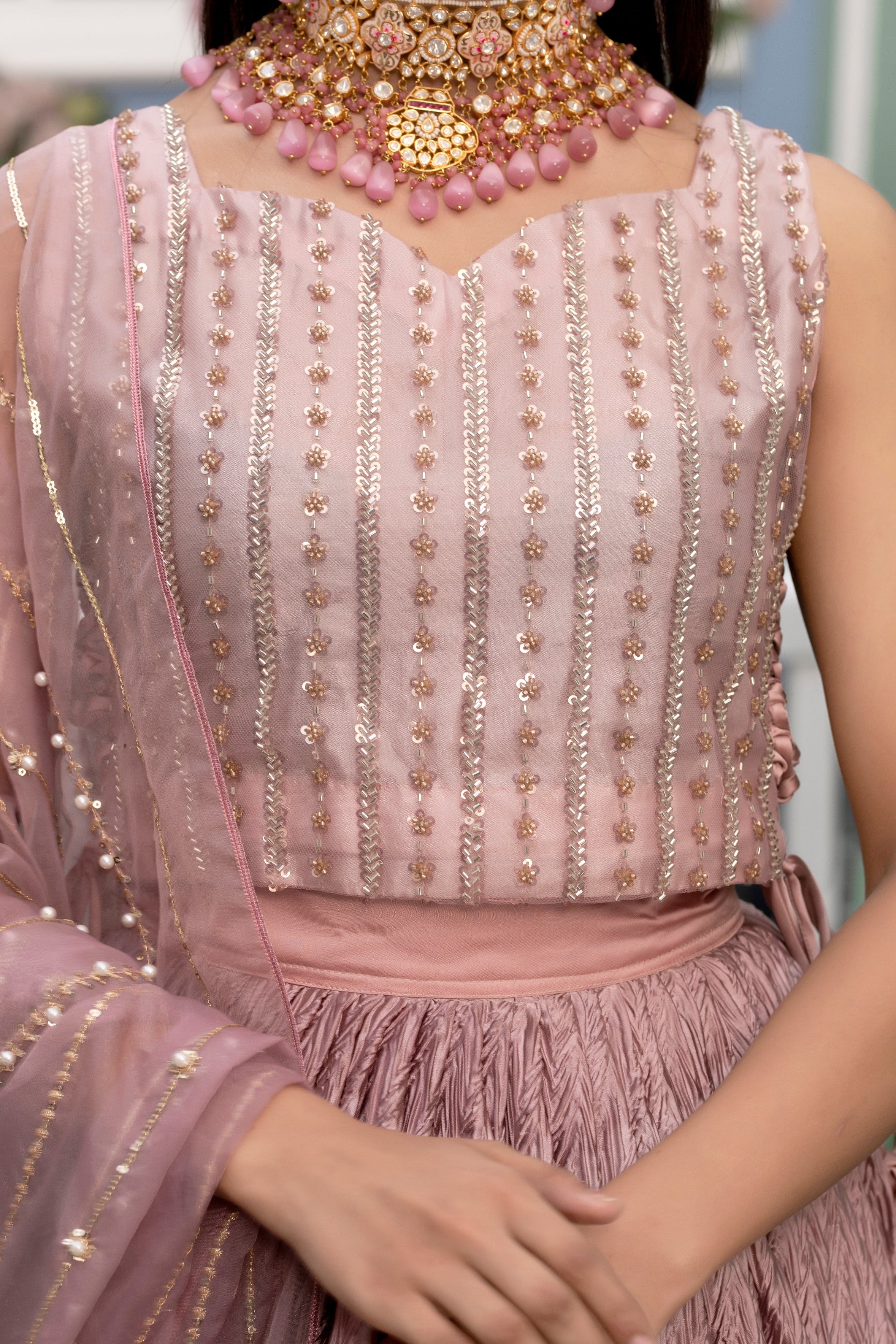 Pink embroidered outfit with gold details and a necklace.