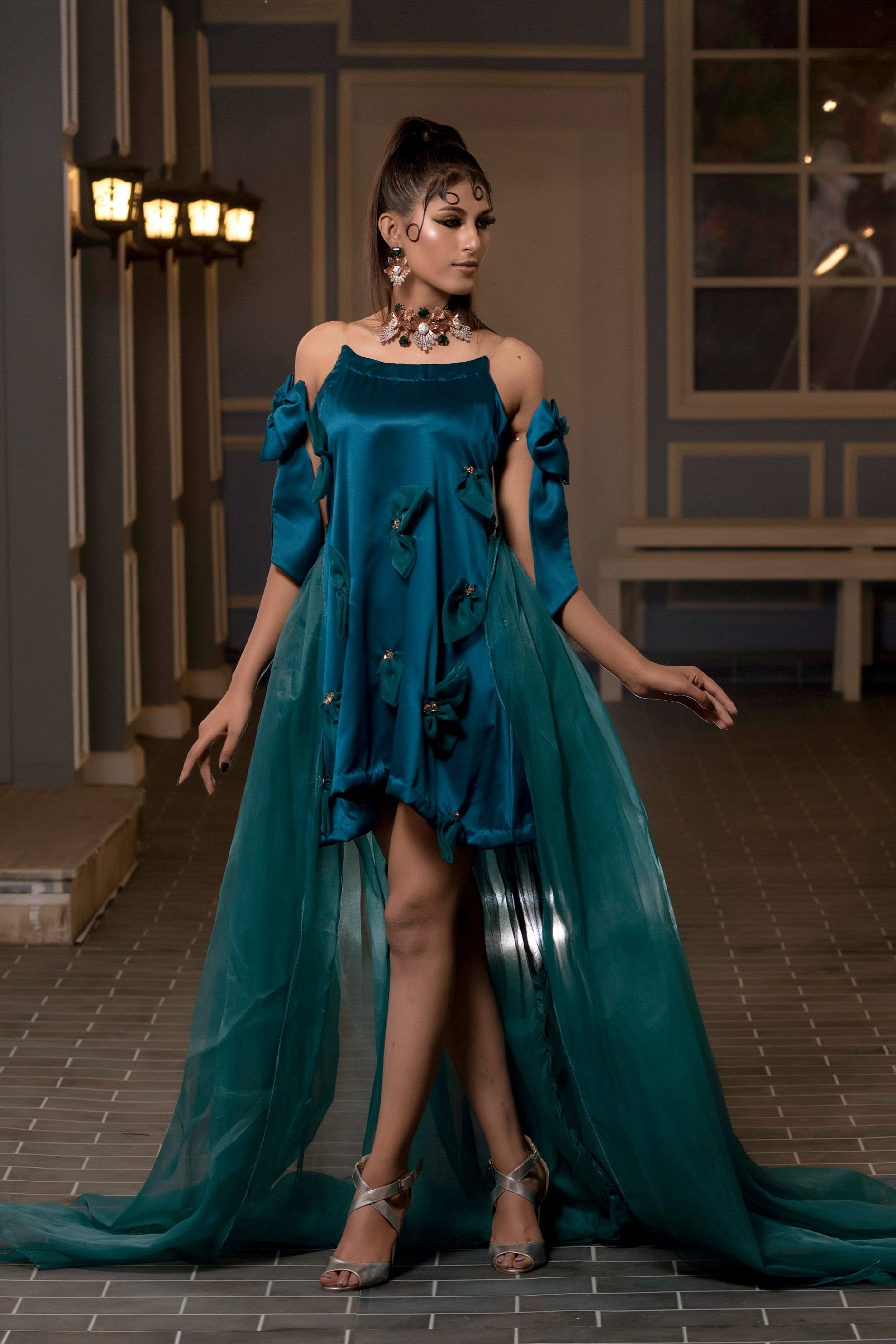 Woman in a teal dress standing in an indoor setting with decorative elements.