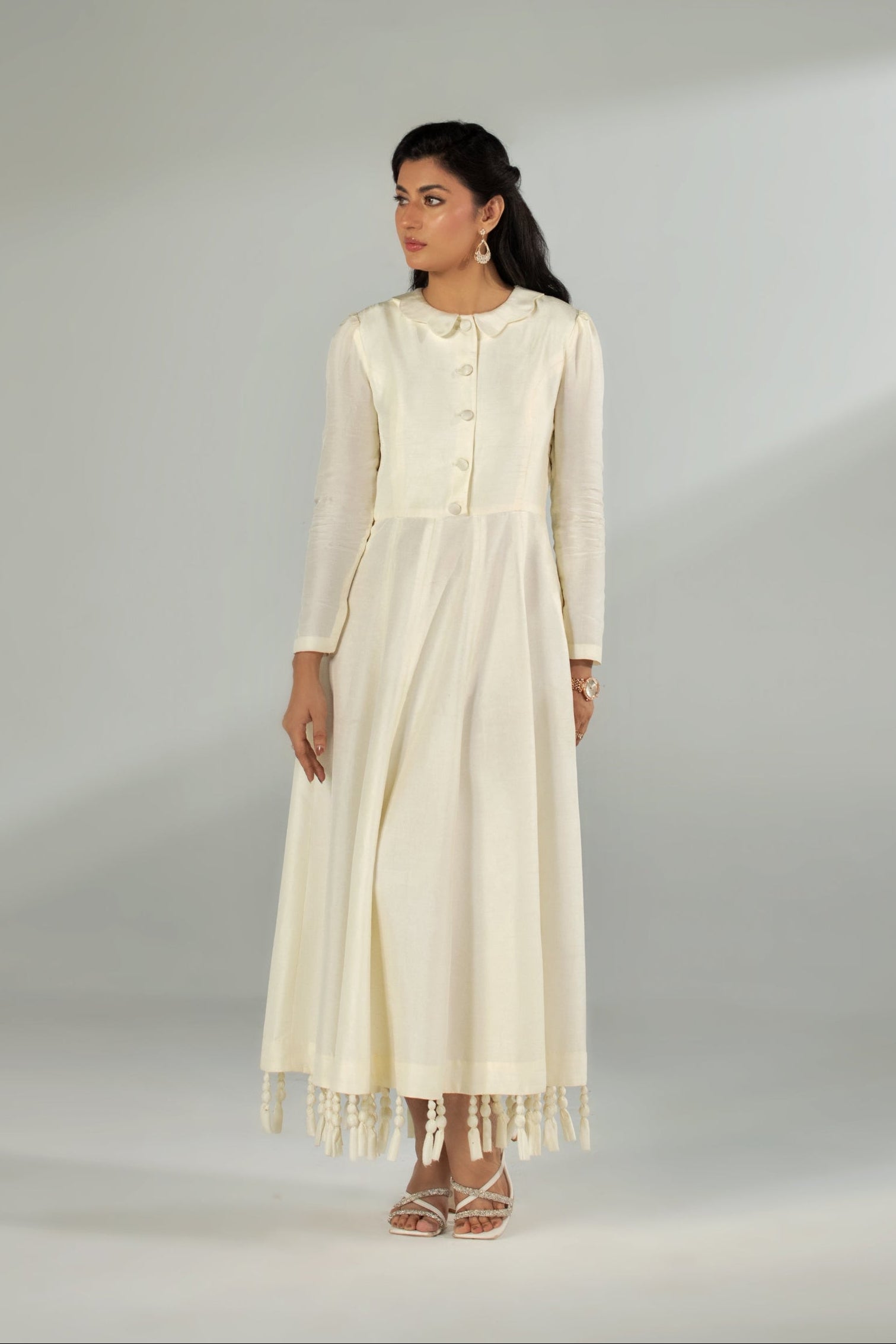 Woman wearing a long, light-colored dress with a plain background