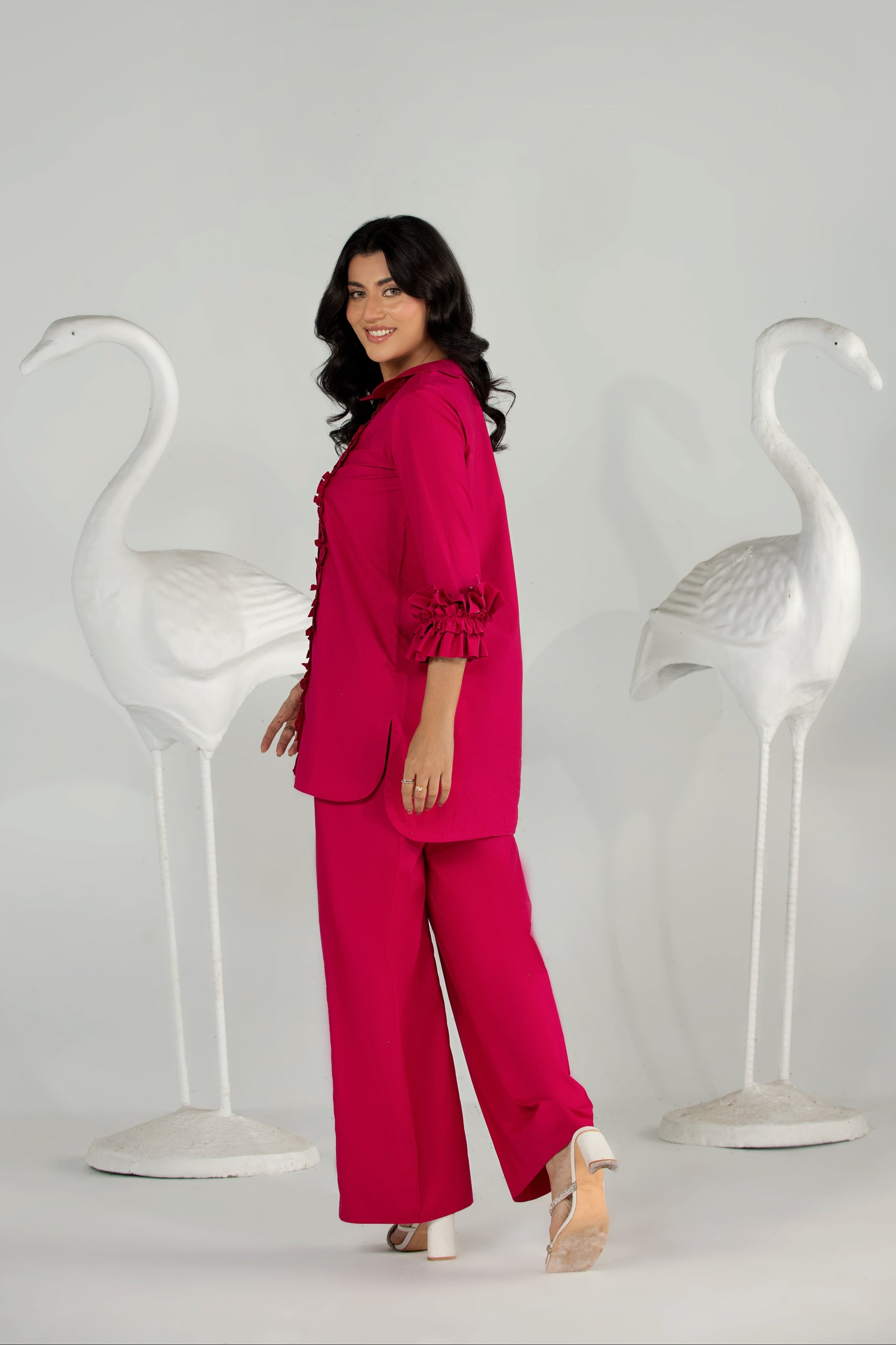 Woman in a pink outfit standing between two white flamingo statues on a plain background