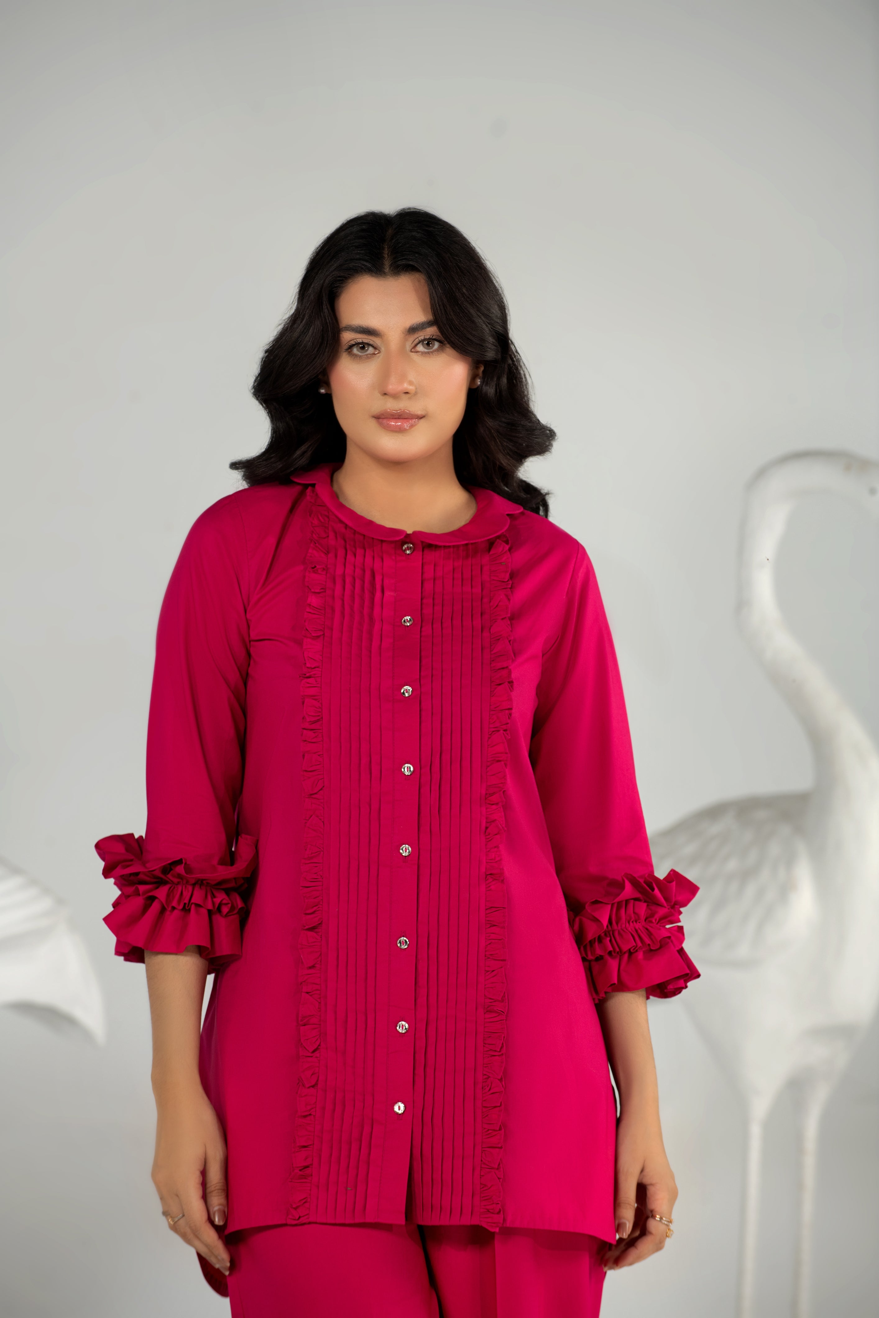 Woman wearing a pink outfit with ruffled details against a white background