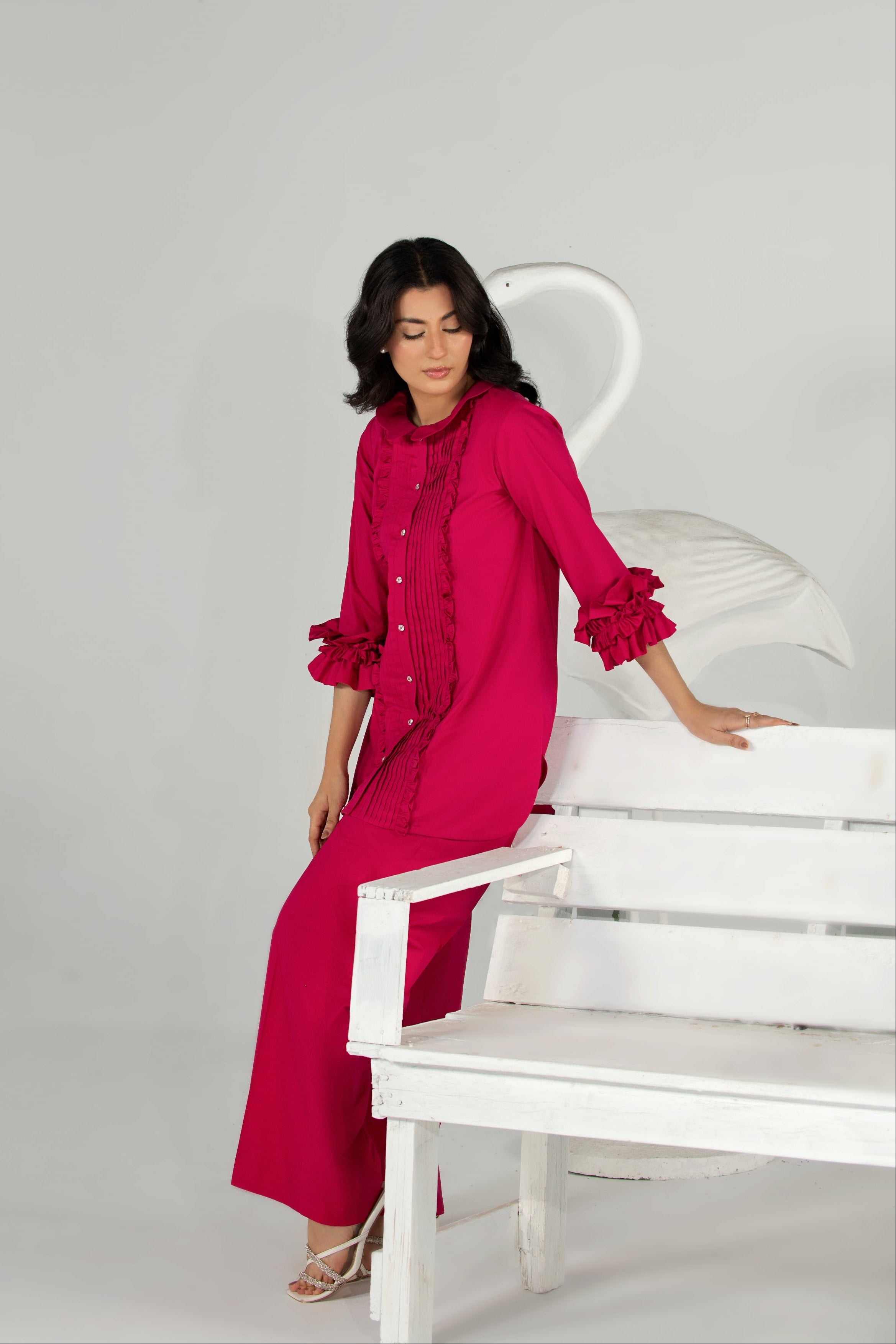 Woman in a bright pink dress sitting on a white chair against a gray background