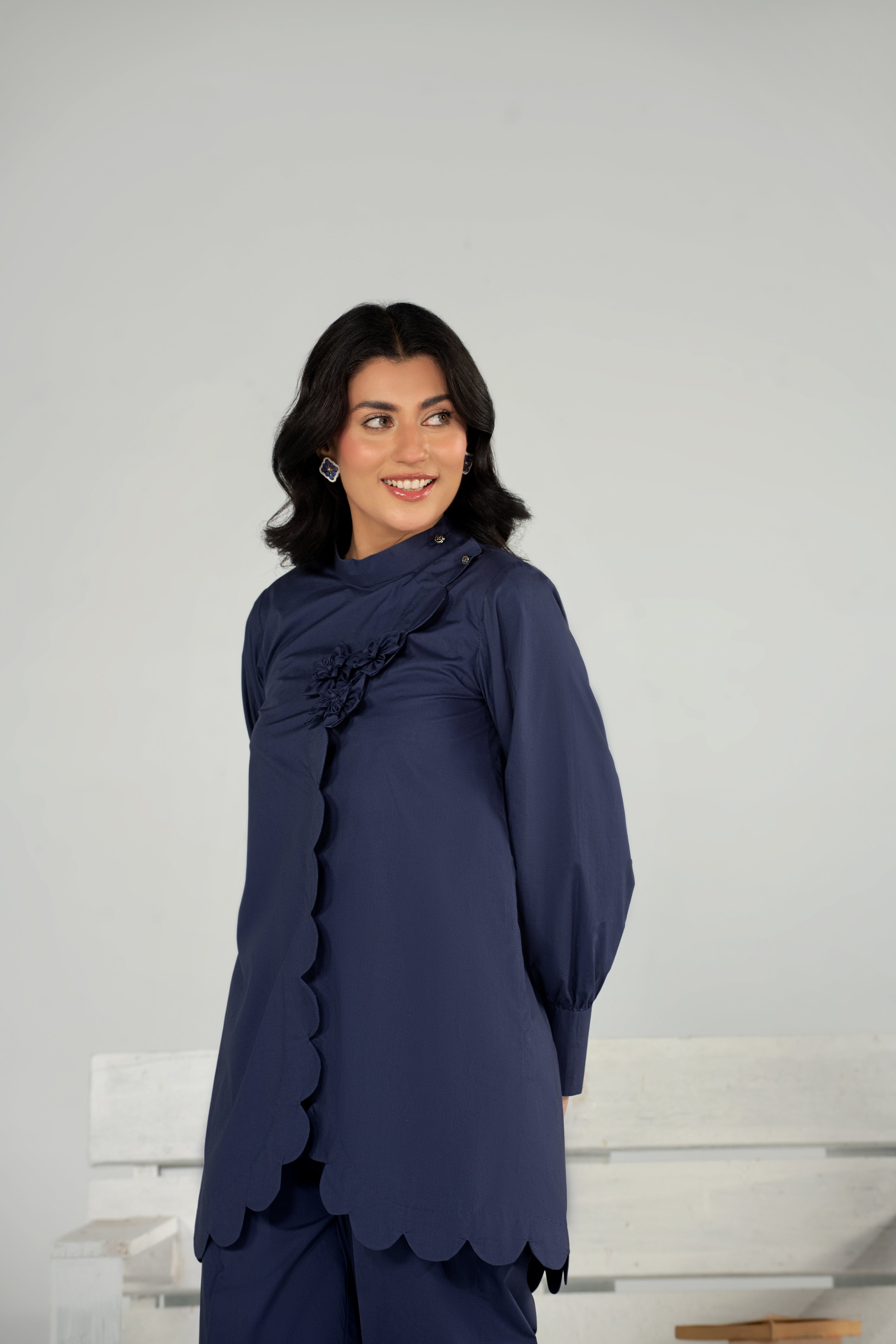 Woman wearing a navy blue outfit with ruffled details against a white background