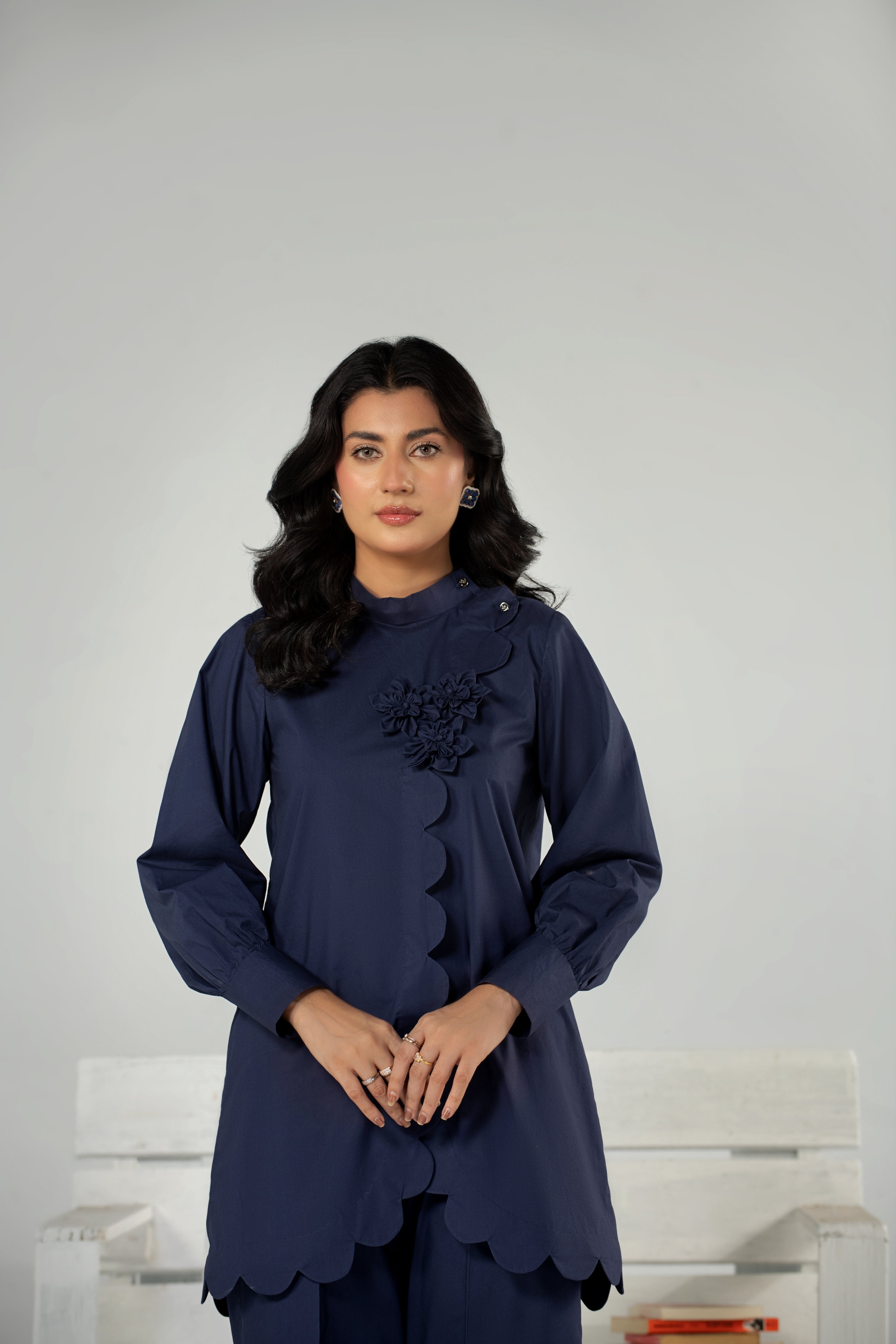 Woman wearing a dark blue outfit with floral details against a plain background