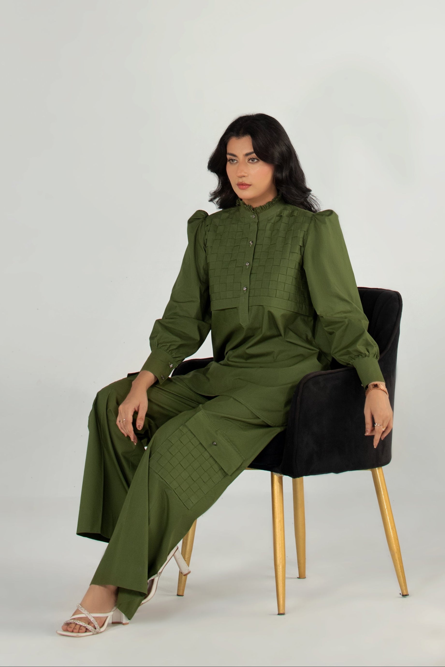 Woman wearing a green jumpsuit sitting on a black chair against a white background