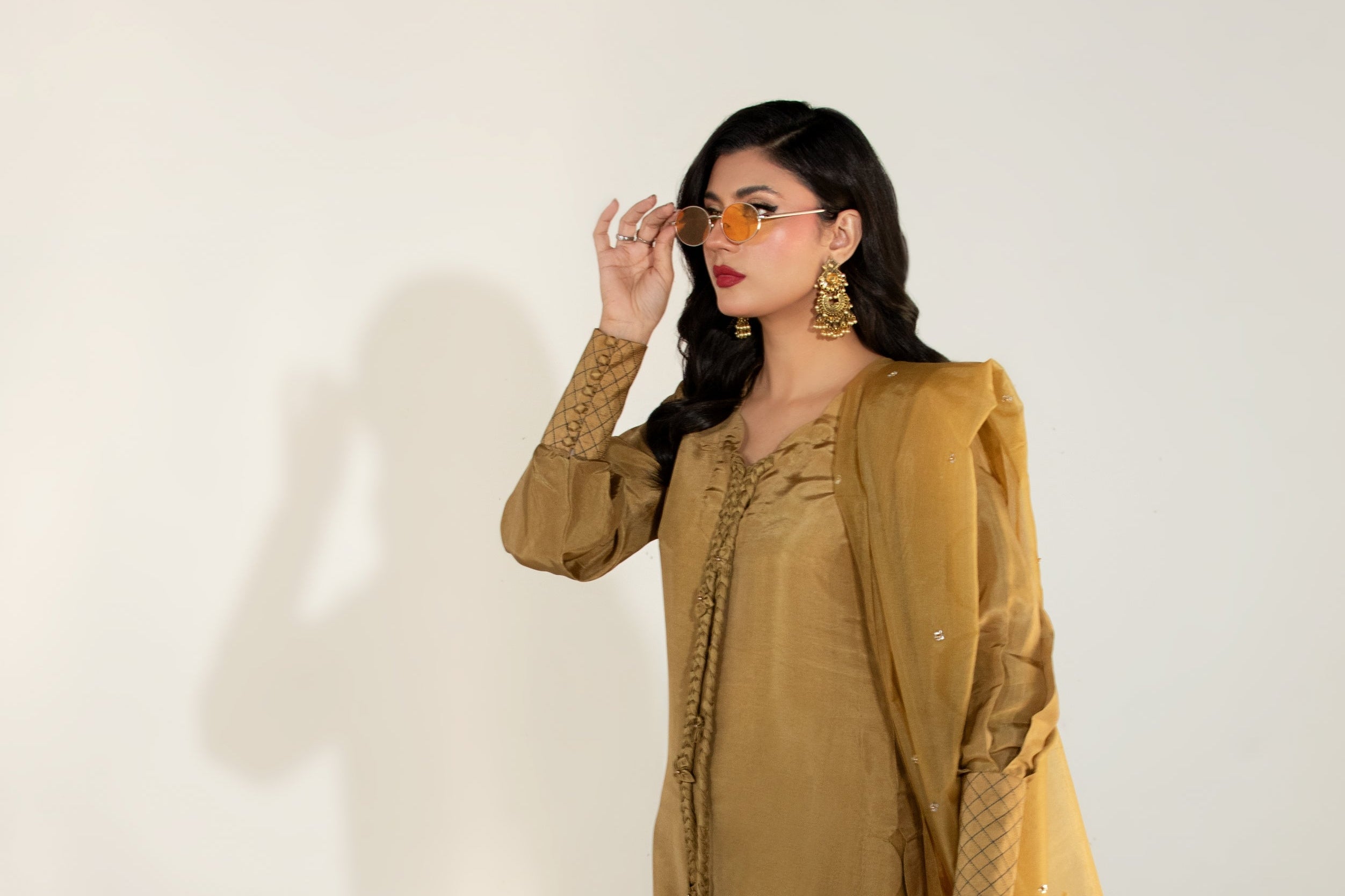Woman wearing a mustard yellow outfit with a long jacket and pants on a white background