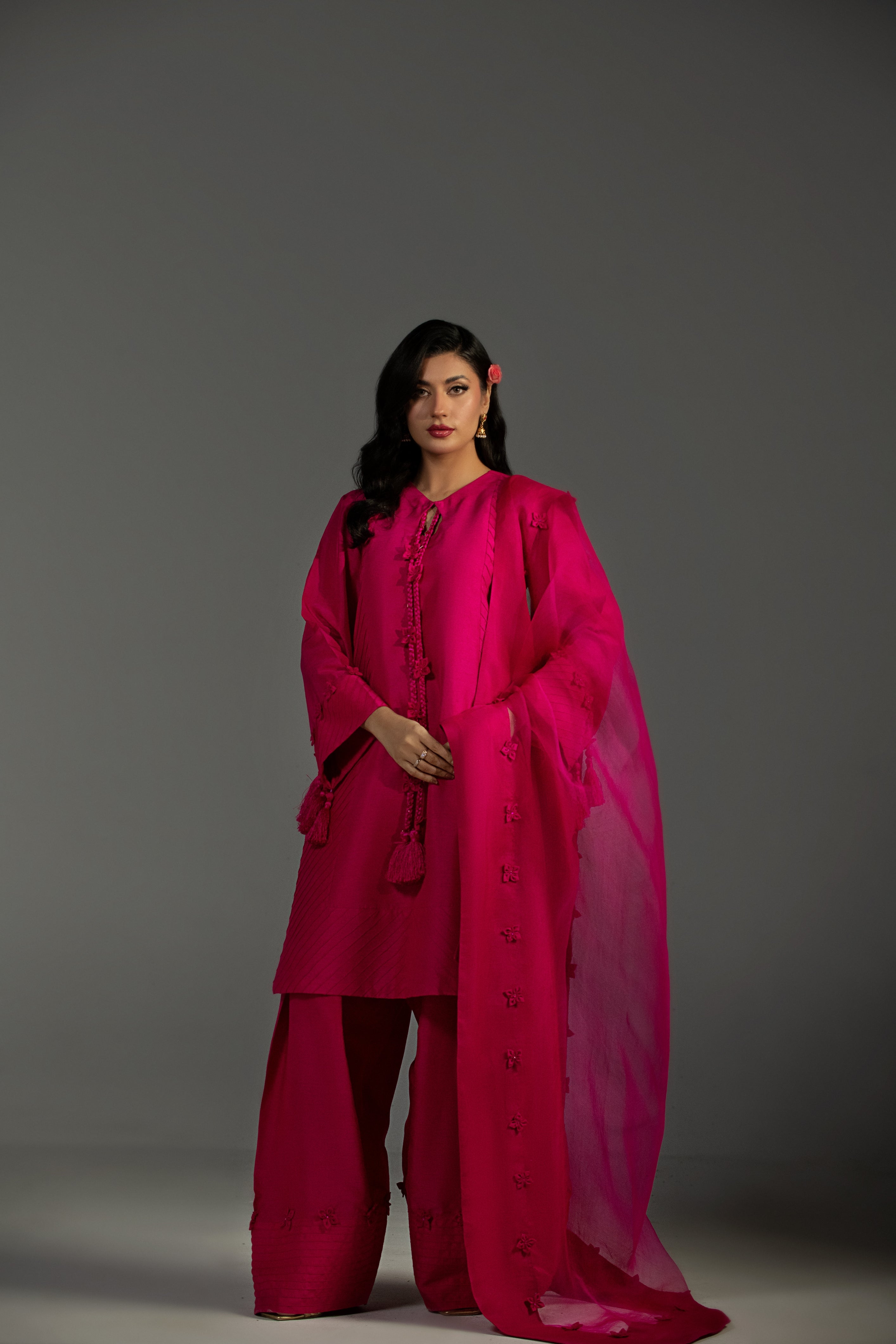 Woman wearing a bright pink traditional outfit with a matching dupatta against a gray background