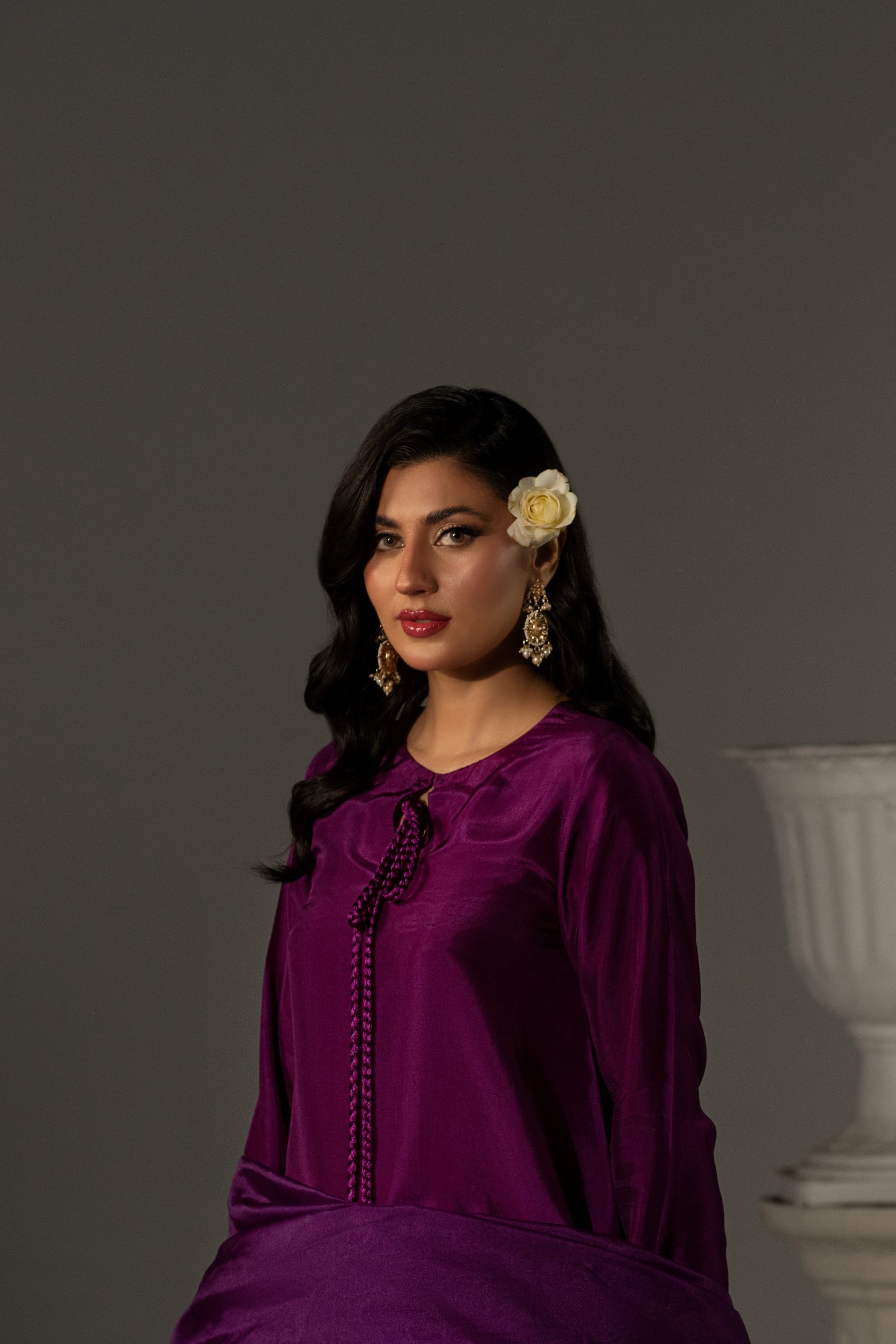 Woman in a purple outfit with a white vase against a gray background