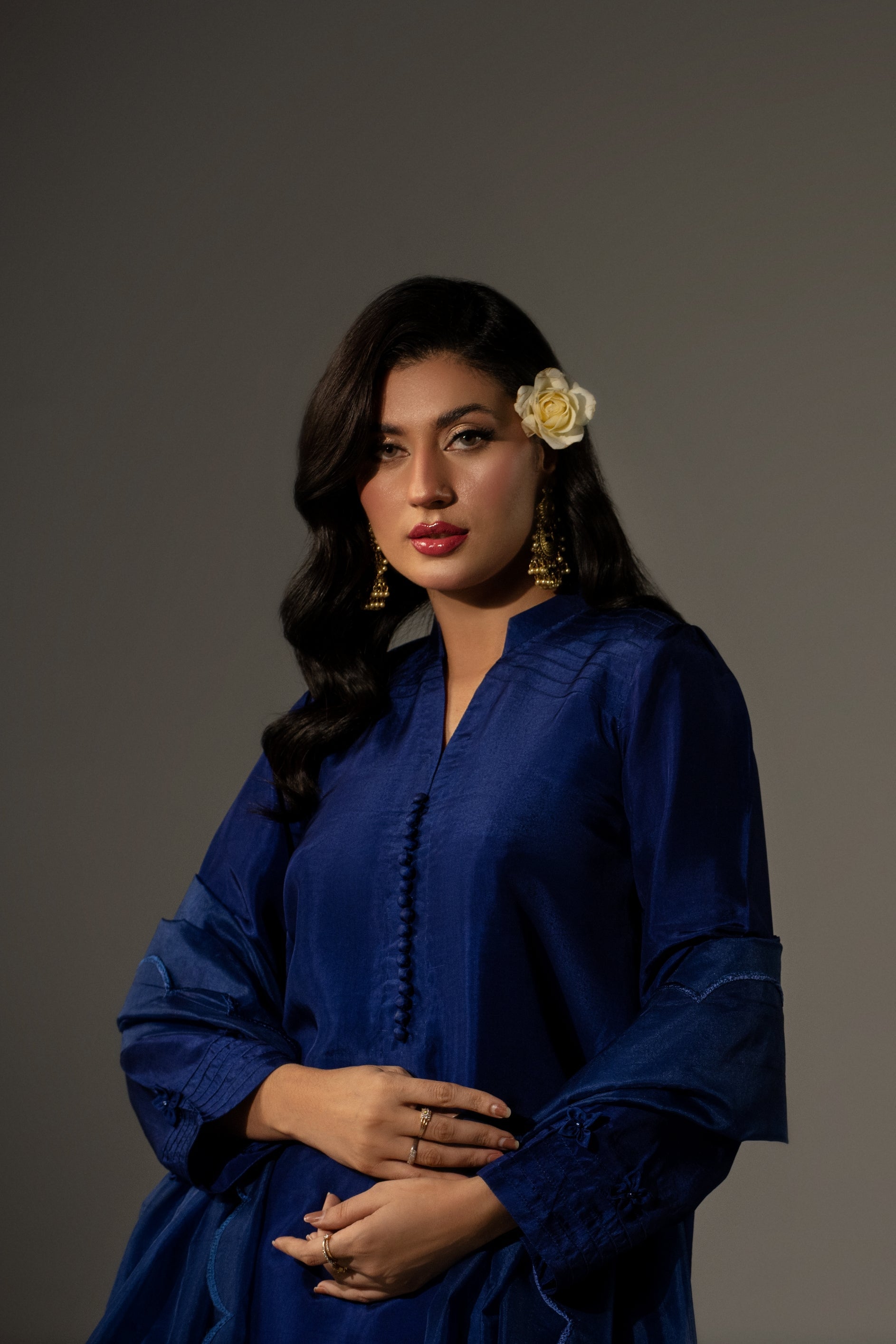 Woman in a blue dress with a flower in her hair against a plain background