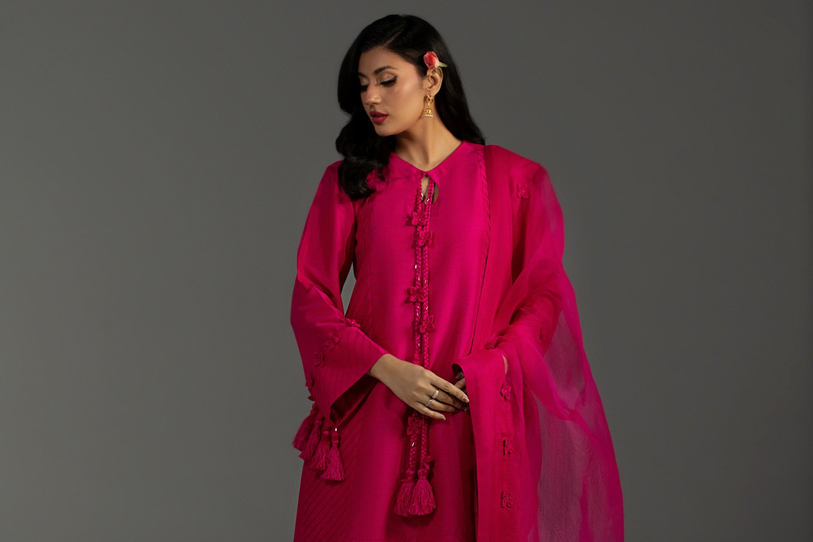 Woman wearing a bright pink traditional outfit with a shawl against a gray background