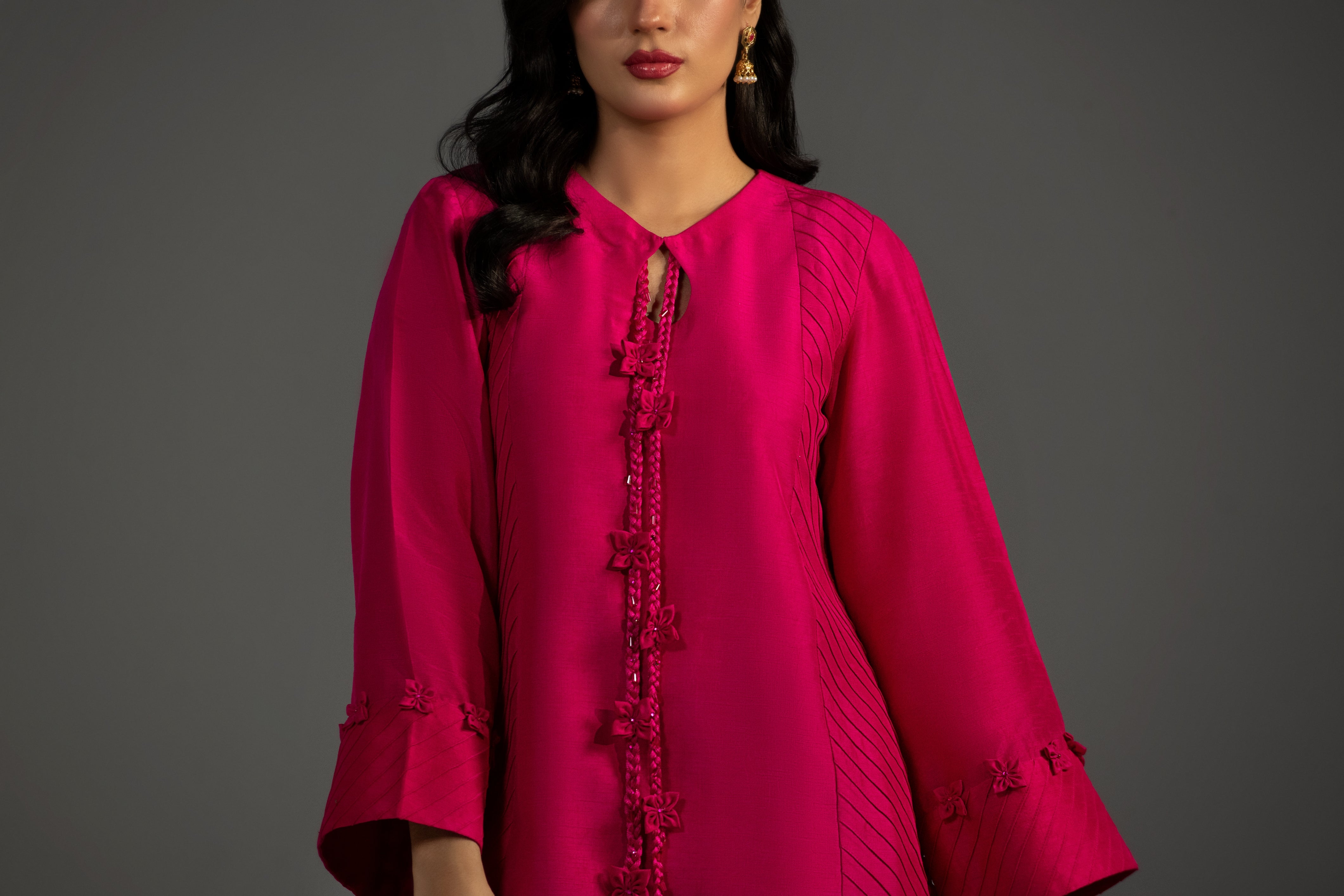 Woman wearing a bright pink traditional outfit with intricate designs on a gray background