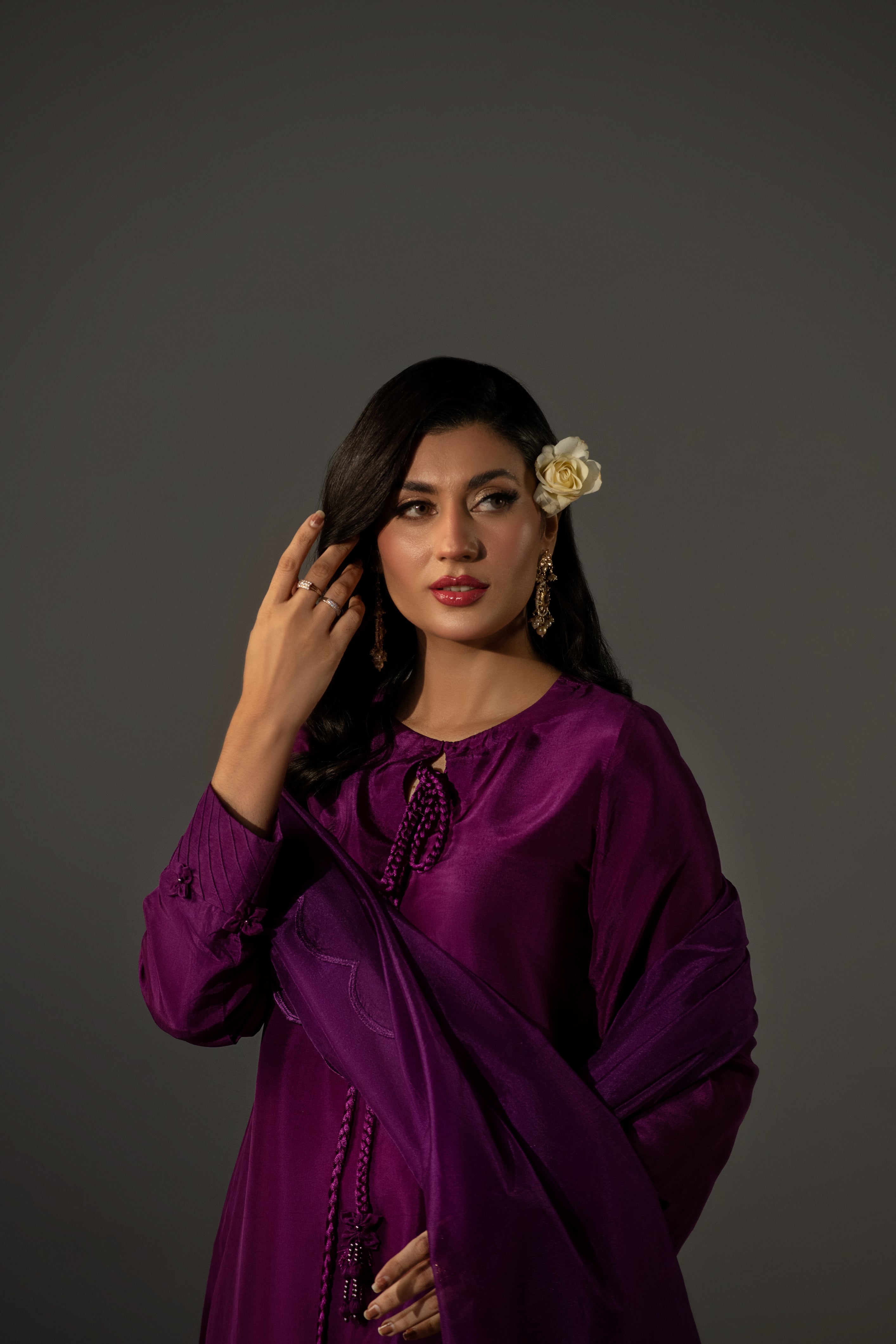 Woman in a purple traditional outfit with a flower in her hair against a gray background