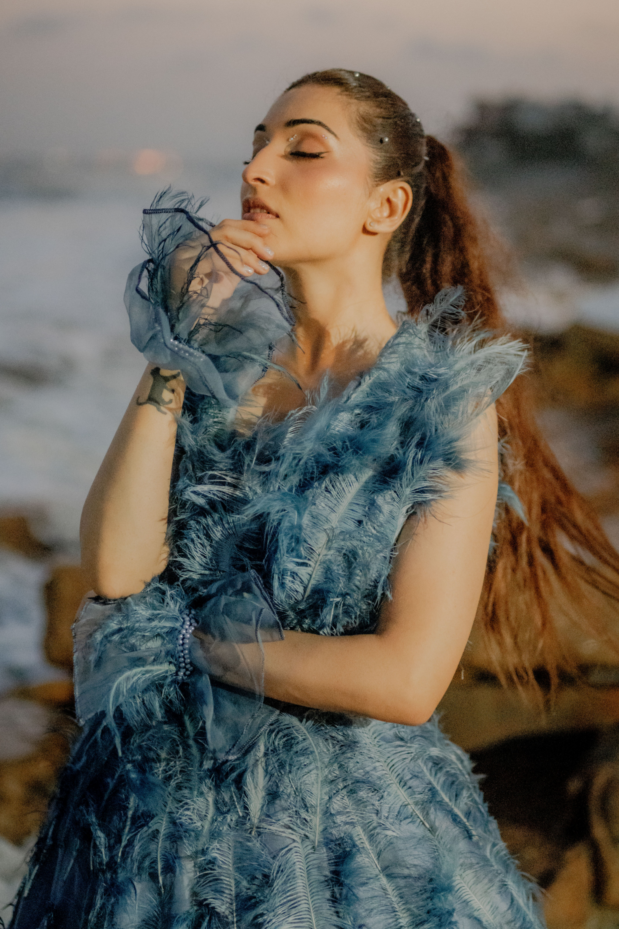 Woman in a blue feathered dress standing outdoors with a blurred background